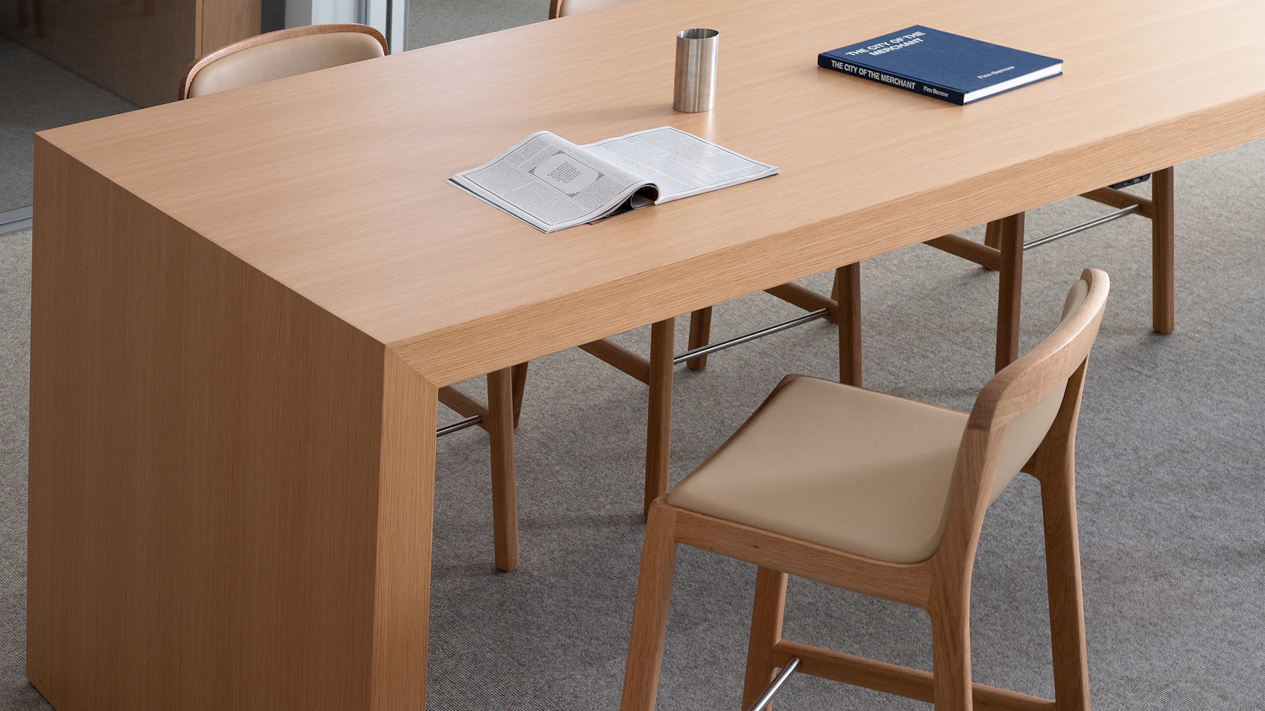 JD Waterfall Table in Natural Rift Cut Oak with four counter height Lijn Stools in Natural Oak fully upholstered with Bristol leather in Champagne, viewed from above at an angle in an office setting.