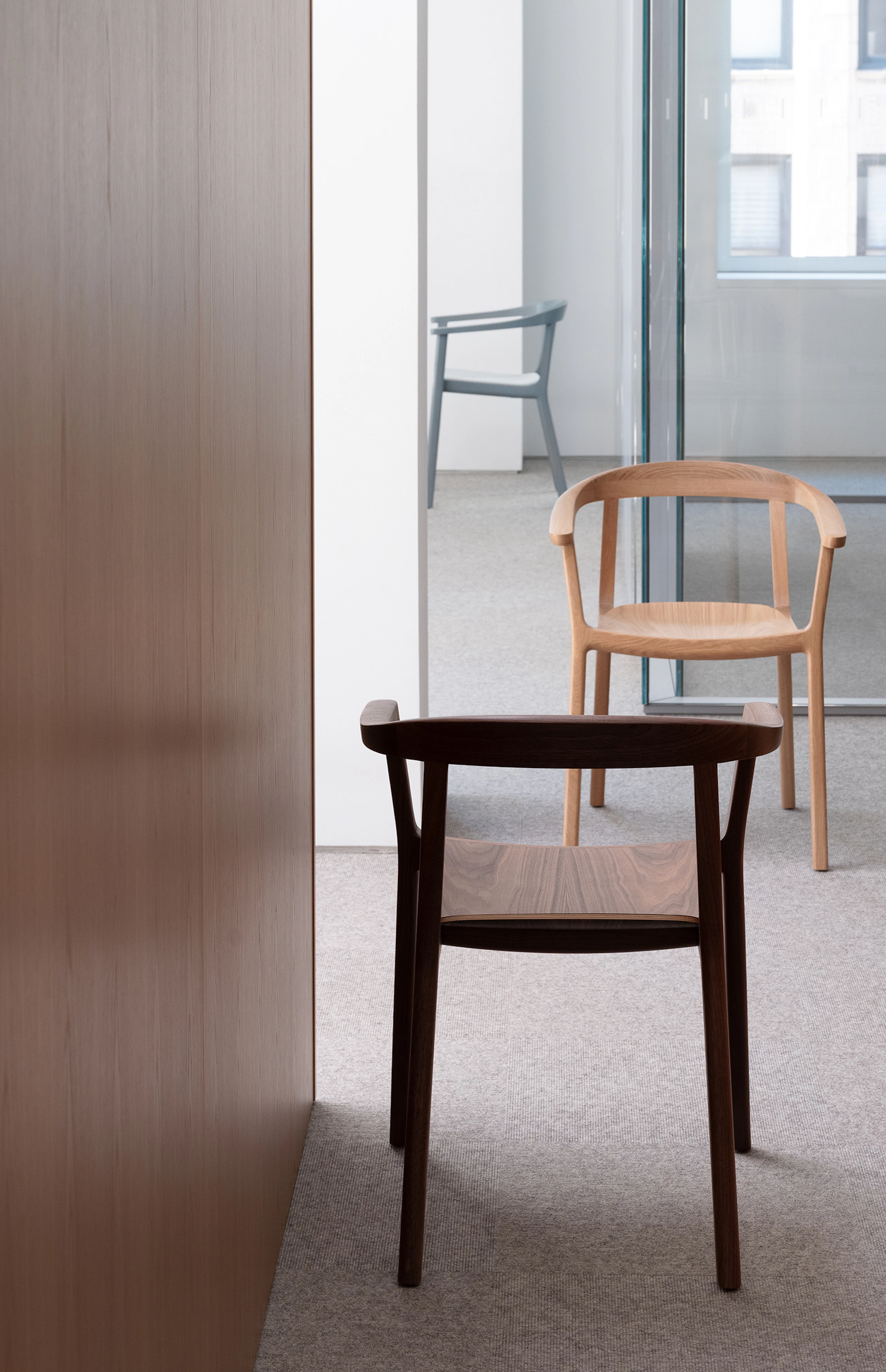 Three Lijn Armchairs in Natural Walnut, Natural Oak, and Nordic Blue, positioned in varying angles in a showroom setting.