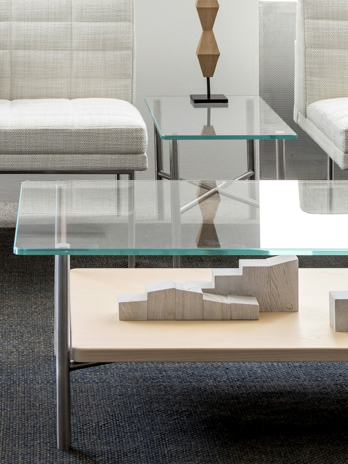 A lounge featuring a rectangular Layer coffee table with a glass top and wood shelf; complemented by off-white Tuxedo Component Lounge Seating.