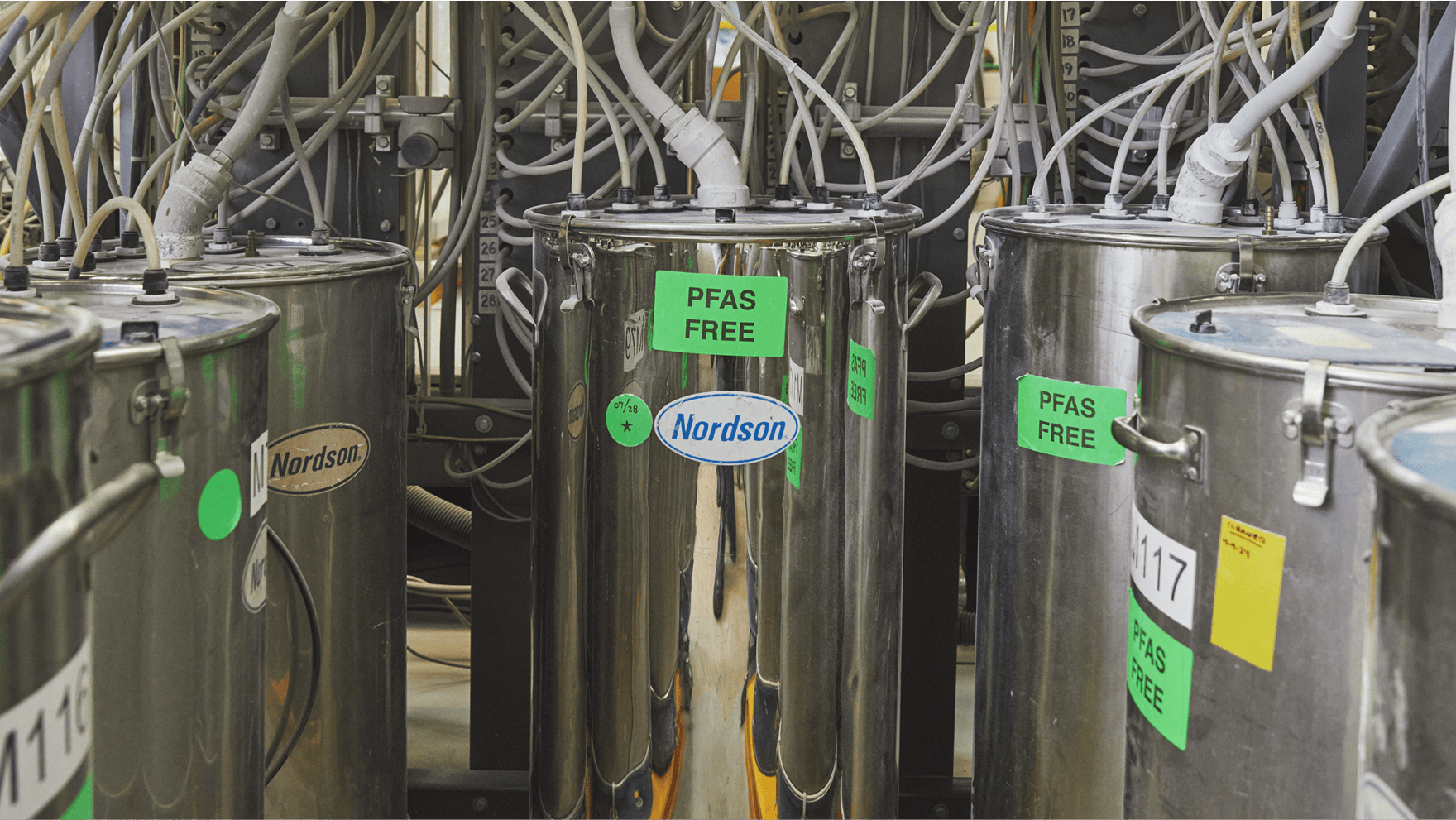 Several large, silver Nordson brand chemical tanks with green stickers that read PFAS FREE.