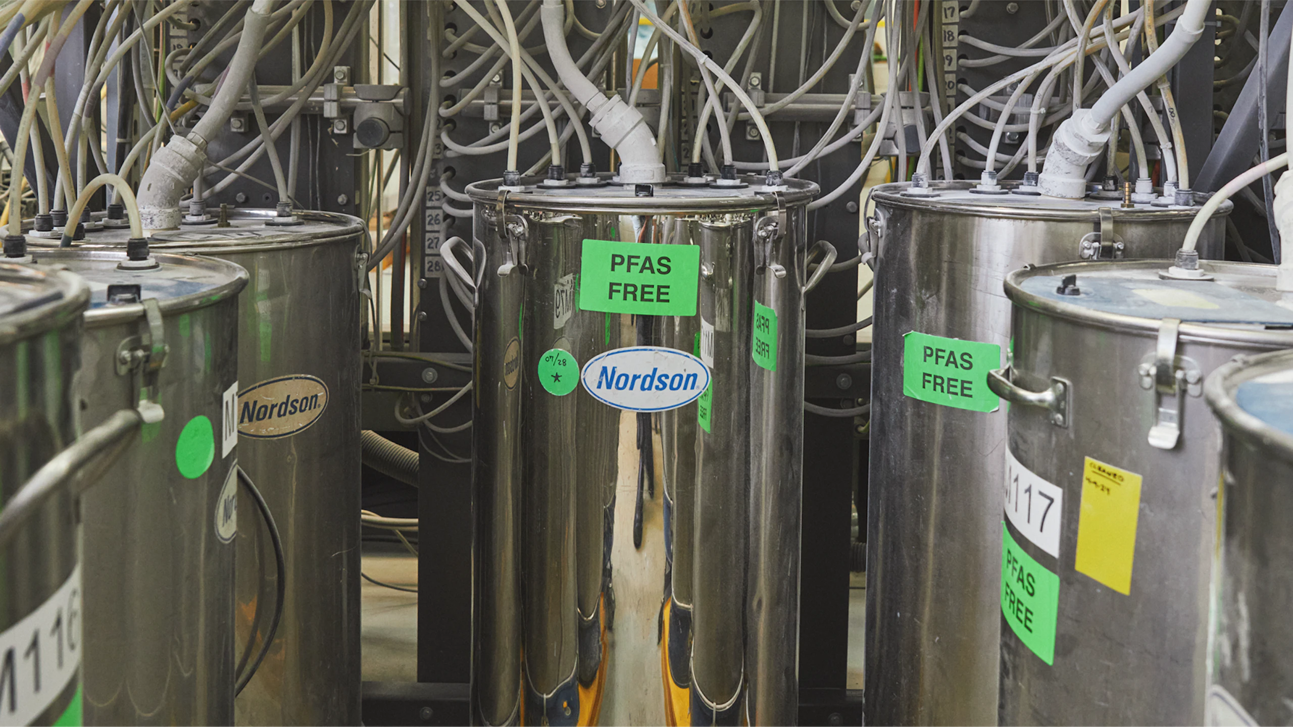Several large, silver Nordson brand chemical tanks with green stickers that read PFAS FREE.