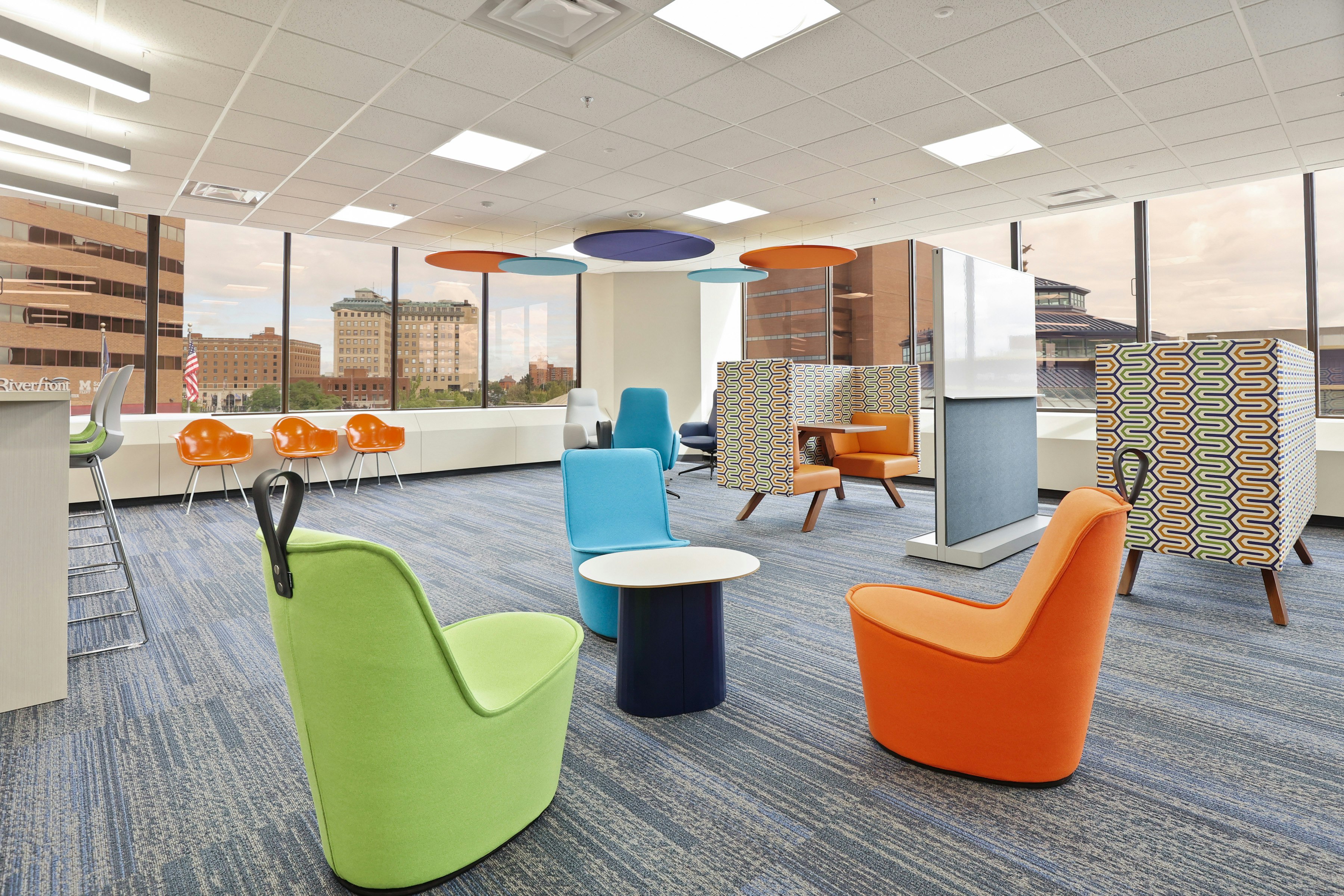 Several colorful group seating areas at the Genesee County administration building furnished with blue, green, and orange NaughtOne Pippin Chairs, orange Eames Molded Plastic Chairs, and semi-private tables.