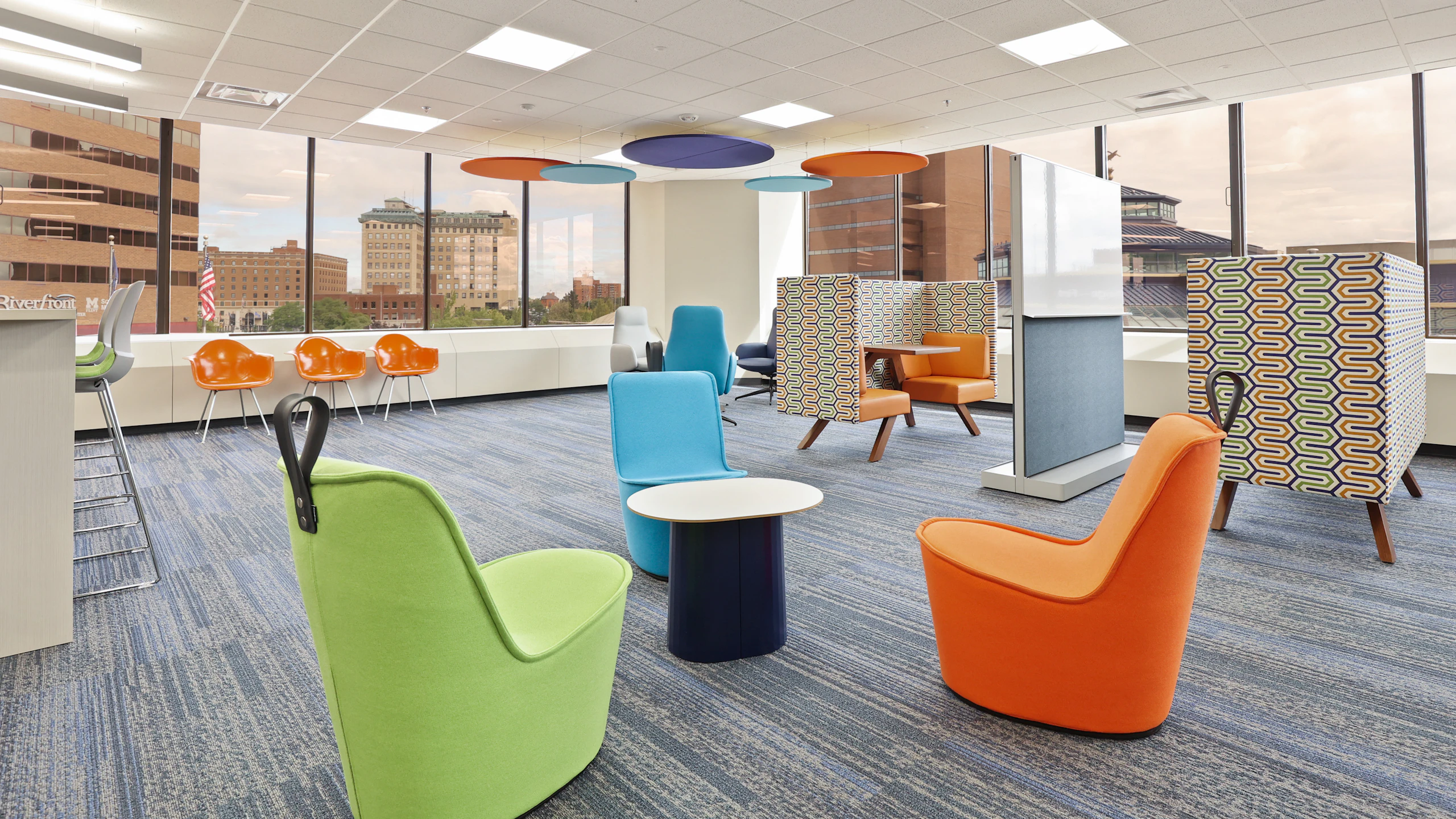 Several colorful group seating areas at the Genesee County administration building furnished with blue, green, and orange NaughtOne Pippin Chairs, orange Eames Molded Plastic Chairs, and semi-private tables.