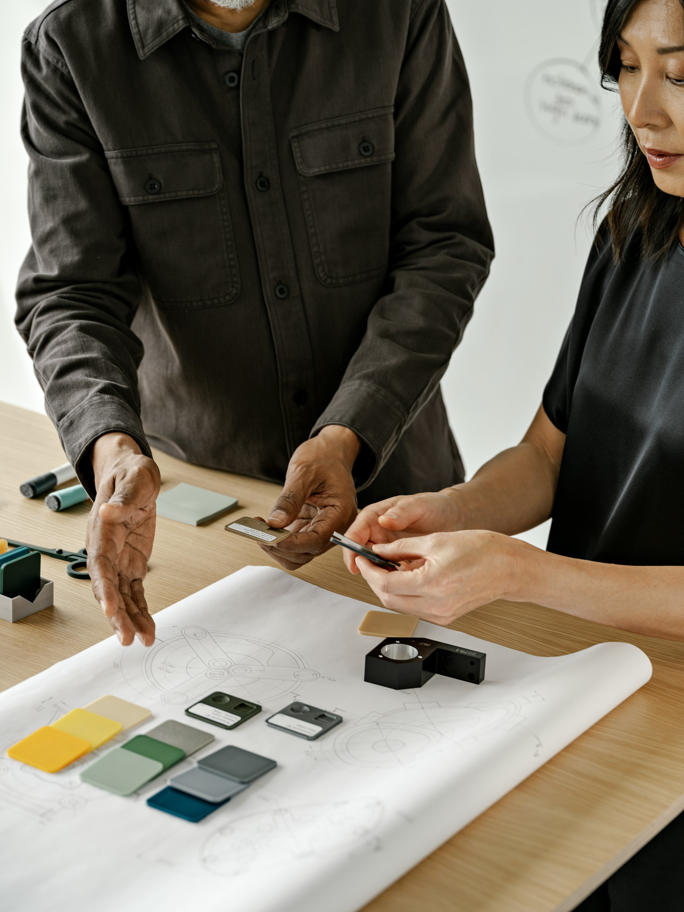 Two people standing at a table discussing a floorplan layout and blue, green, grey, and yellow color swatches.