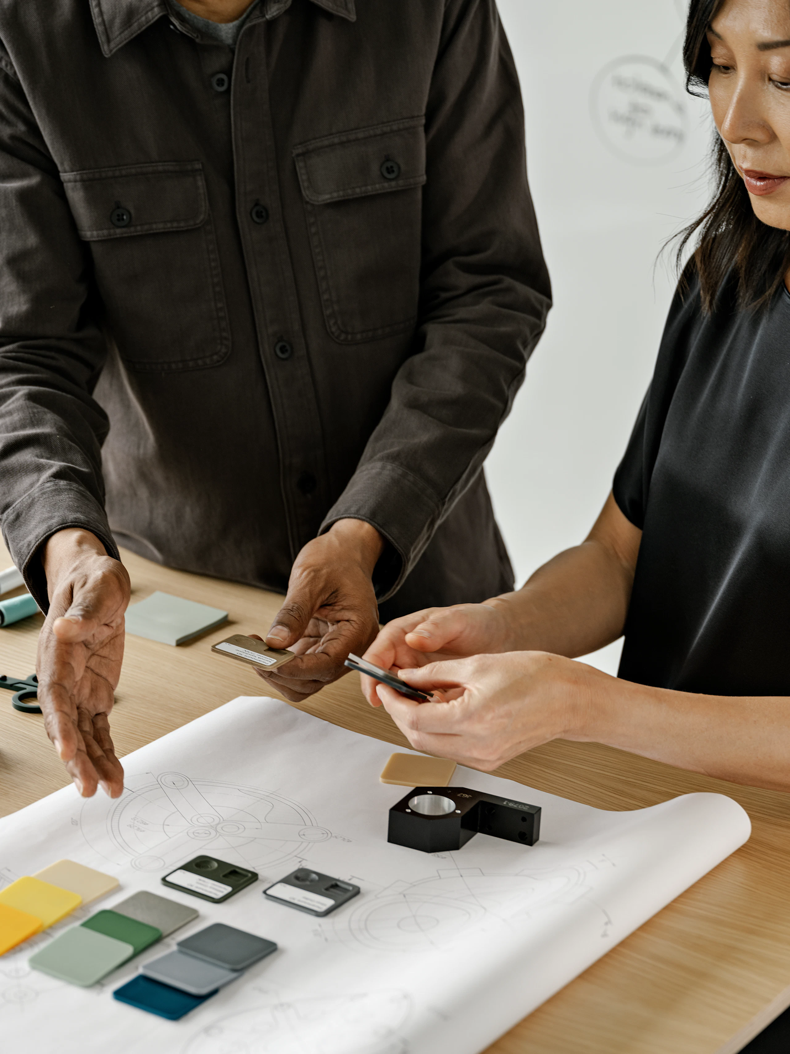 Two people standing at a table discussing a floorplan layout and blue, green, grey, and yellow color swatches.