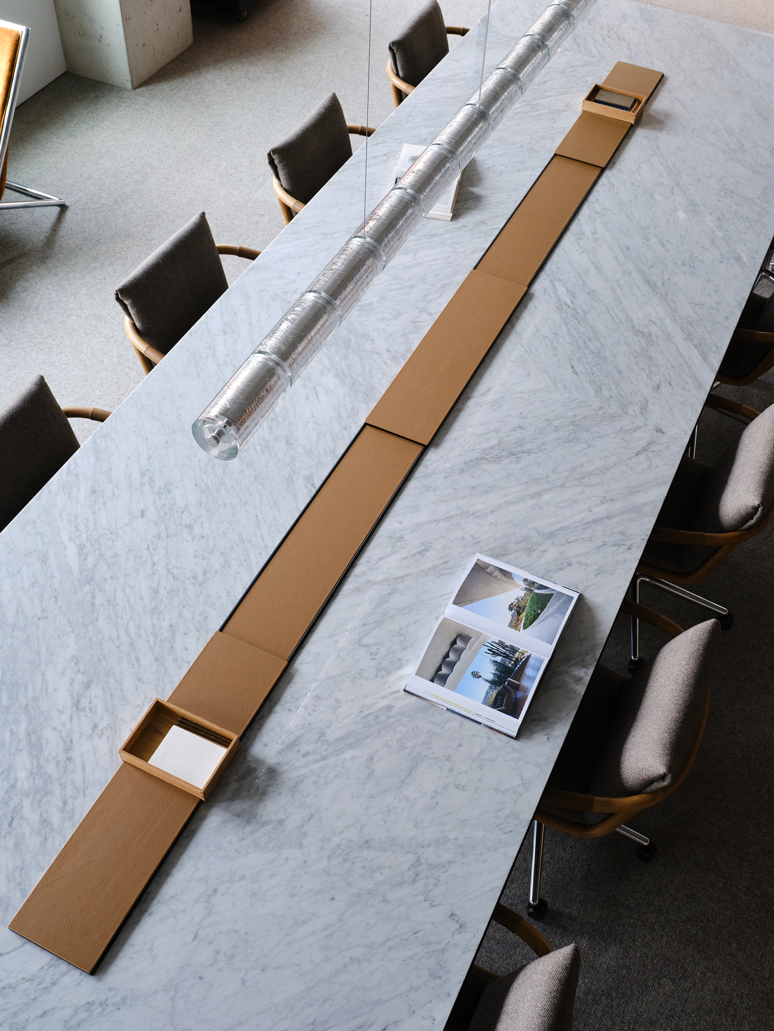 Ascent Conference Table, designed by EOOS, shown in White Carrara Marble with leather-covered power troughs, paired with Full Loop Chairs, viewed from above in an open setting.