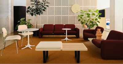 Two red sofa configurations from the Wilkes Modular Sofa Group atop an orange rug and white side tables on display at the Herman Miller showroom at MillerKnoll Design Days