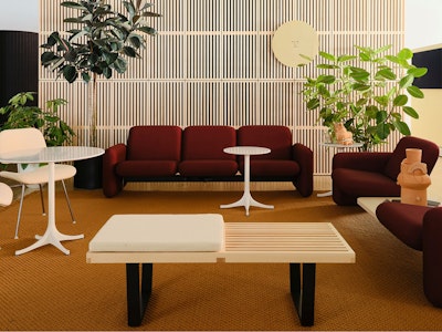 Two red sofa configurations from the Wilkes Modular Sofa Group atop an orange rug and white side tables on display at the Herman Miller showroom at MillerKnoll Design Days