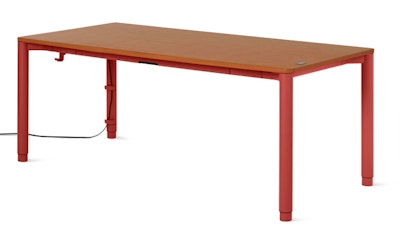 A front three quarter view of a Spout Sit-to-Stand Table from Herman Miller with a wood finish top and Canyon finish legs