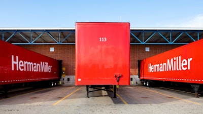 Three red delivery trucks, each featuring the Herman Miller logo on its side.
