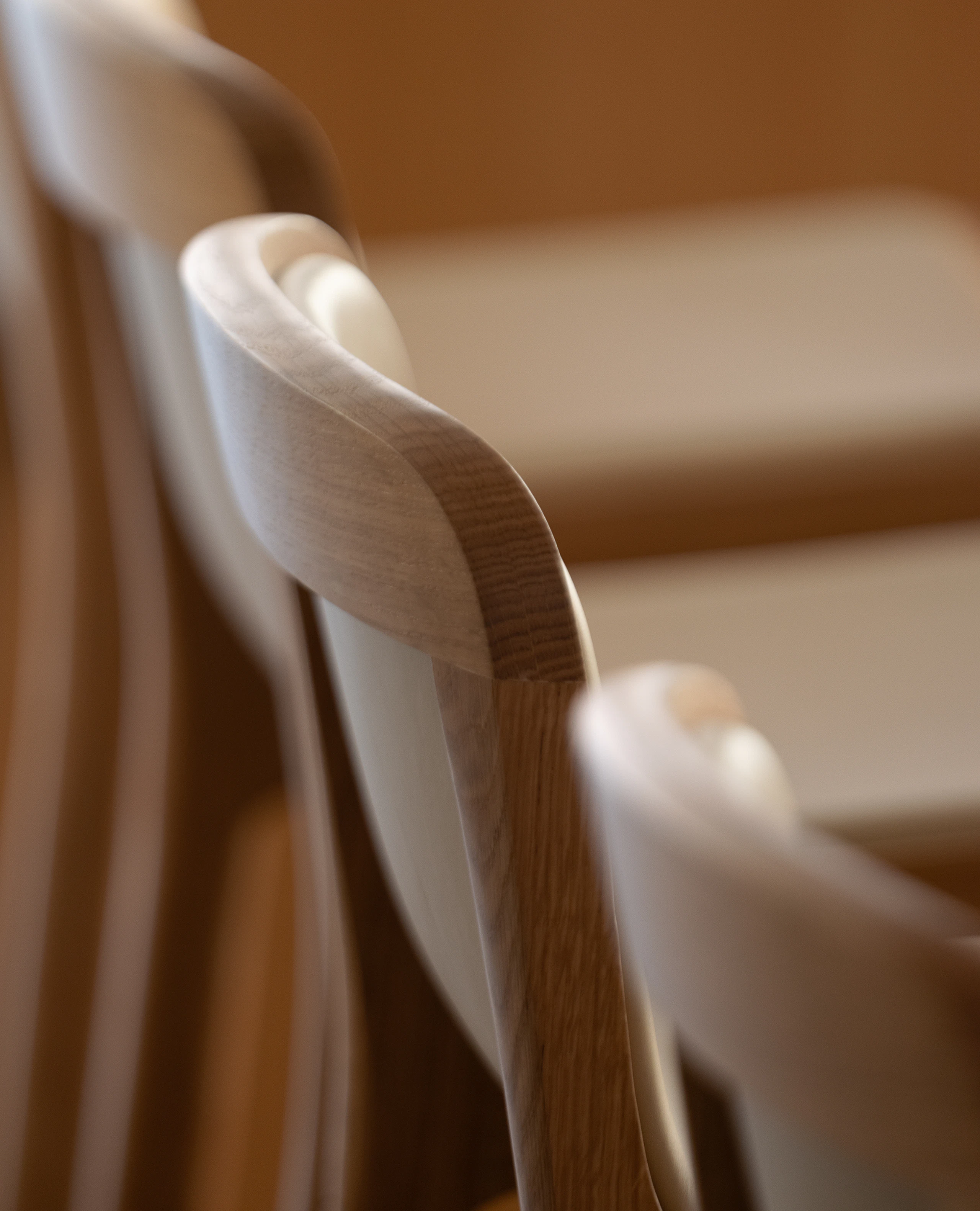 Detail shot of three counter height Lijn Stool seatbacks in Natural Oak, fully upholstered with Bristol Leather in Champagne, viewed from behind at an angle.