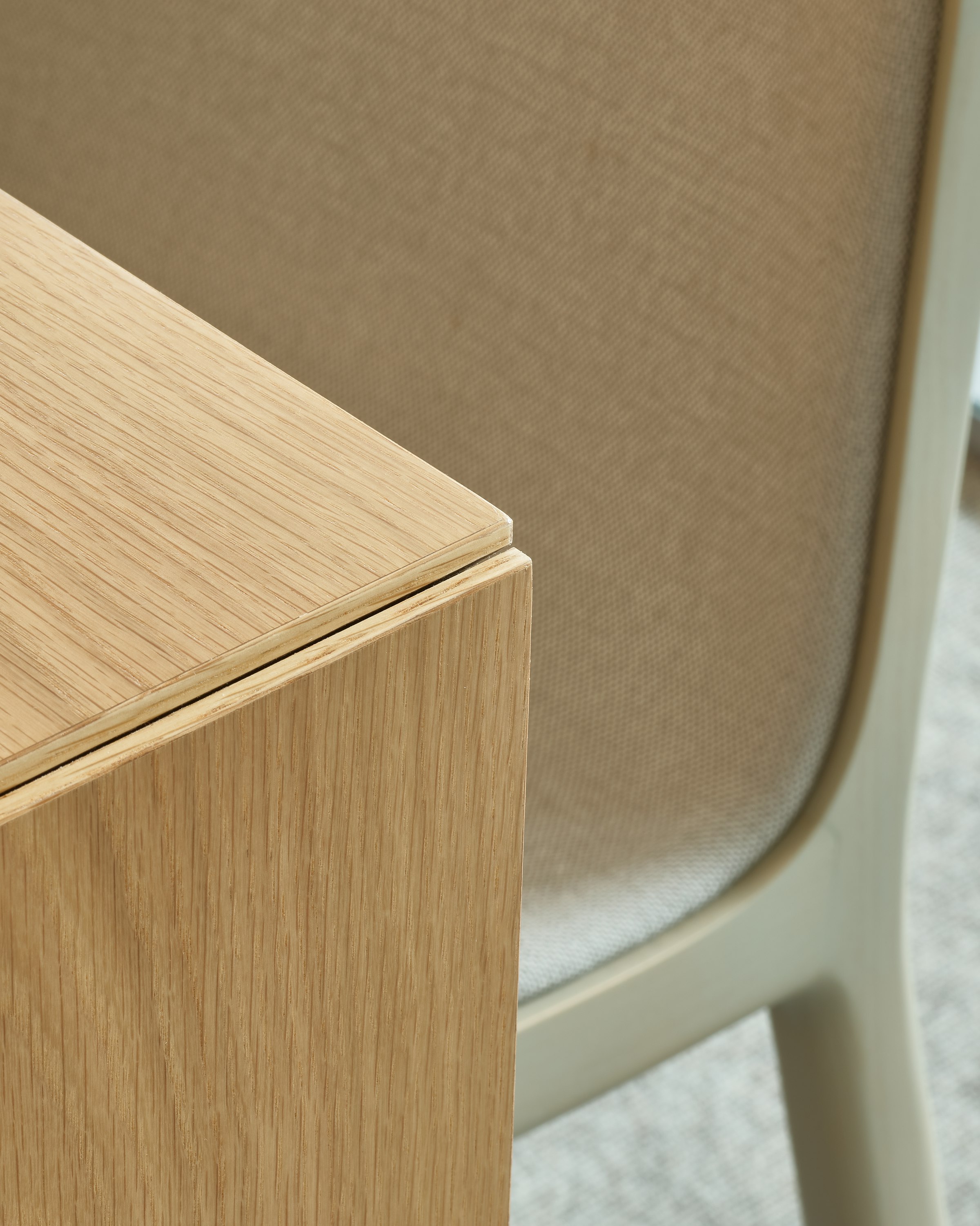 Detail view of a Geiger One Private Office Cascade Leg corner in Natural Flat Cut Oak, with a Lijn Side Chair in the background, viewed at an angle.