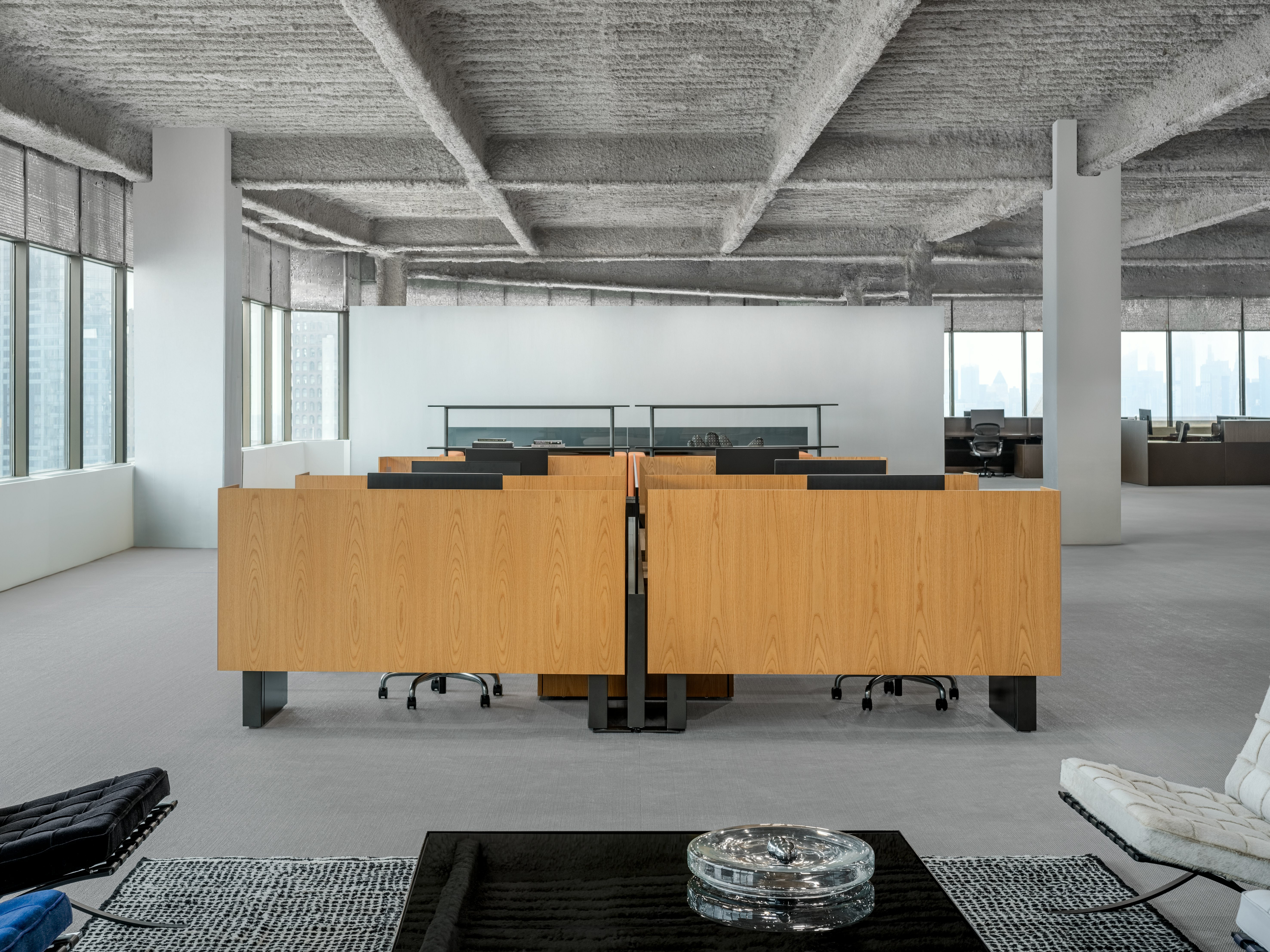A group of workstations in an open office are viewed straight on from a lounge seating area.