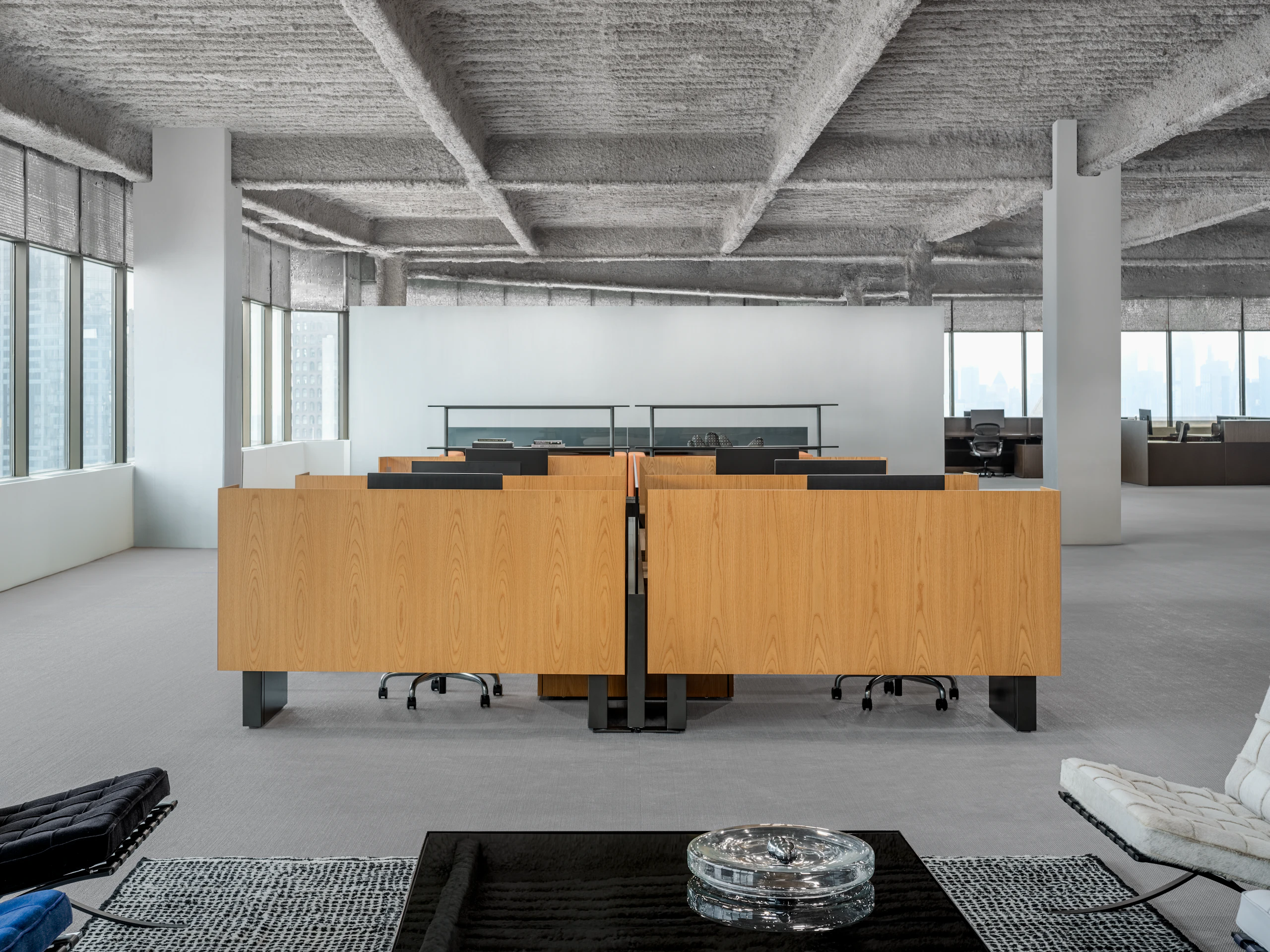 A group of workstations in an open office are viewed straight on from a lounge seating area.