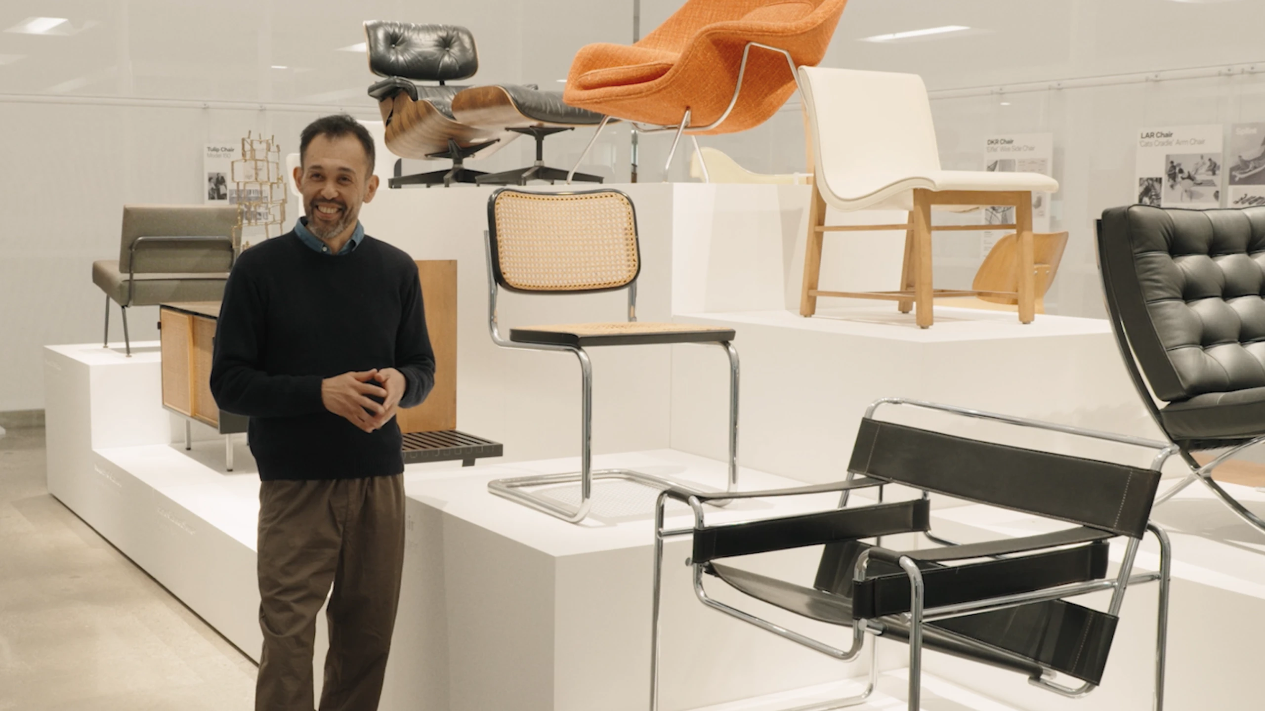 Keiji Takeuchi standing next to a Cesca Chairk, Womb Chair, Eames Chair, and other classic pieces of furniture at the MillerKnoll Archives.