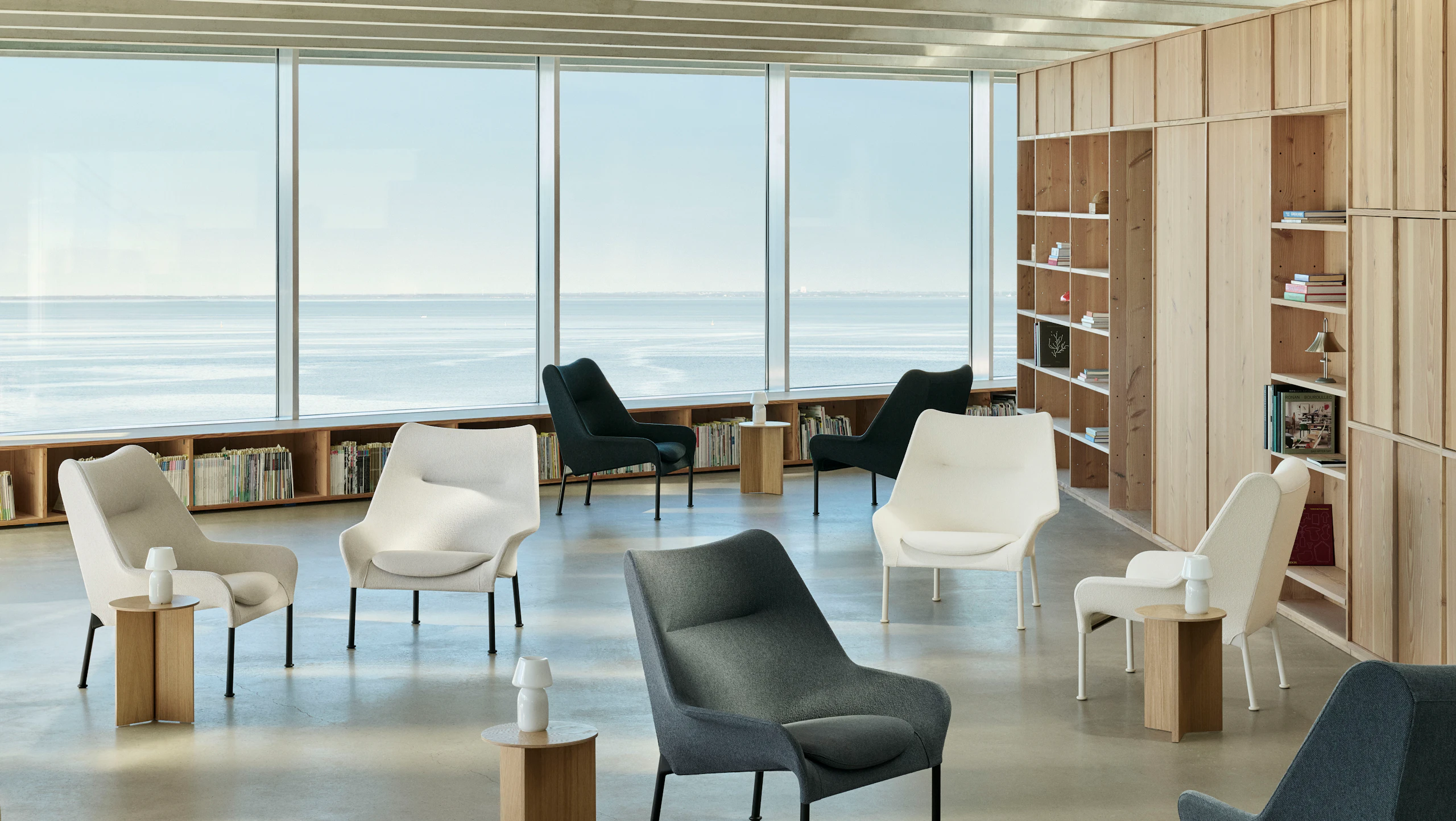 Lifestyle shot of multiple O2 lounge chairs and Wood Slit Tables in a glass-walled workspace.