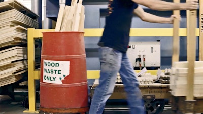 A person walking past a red barrel with a recycling label that reads wood waste only.