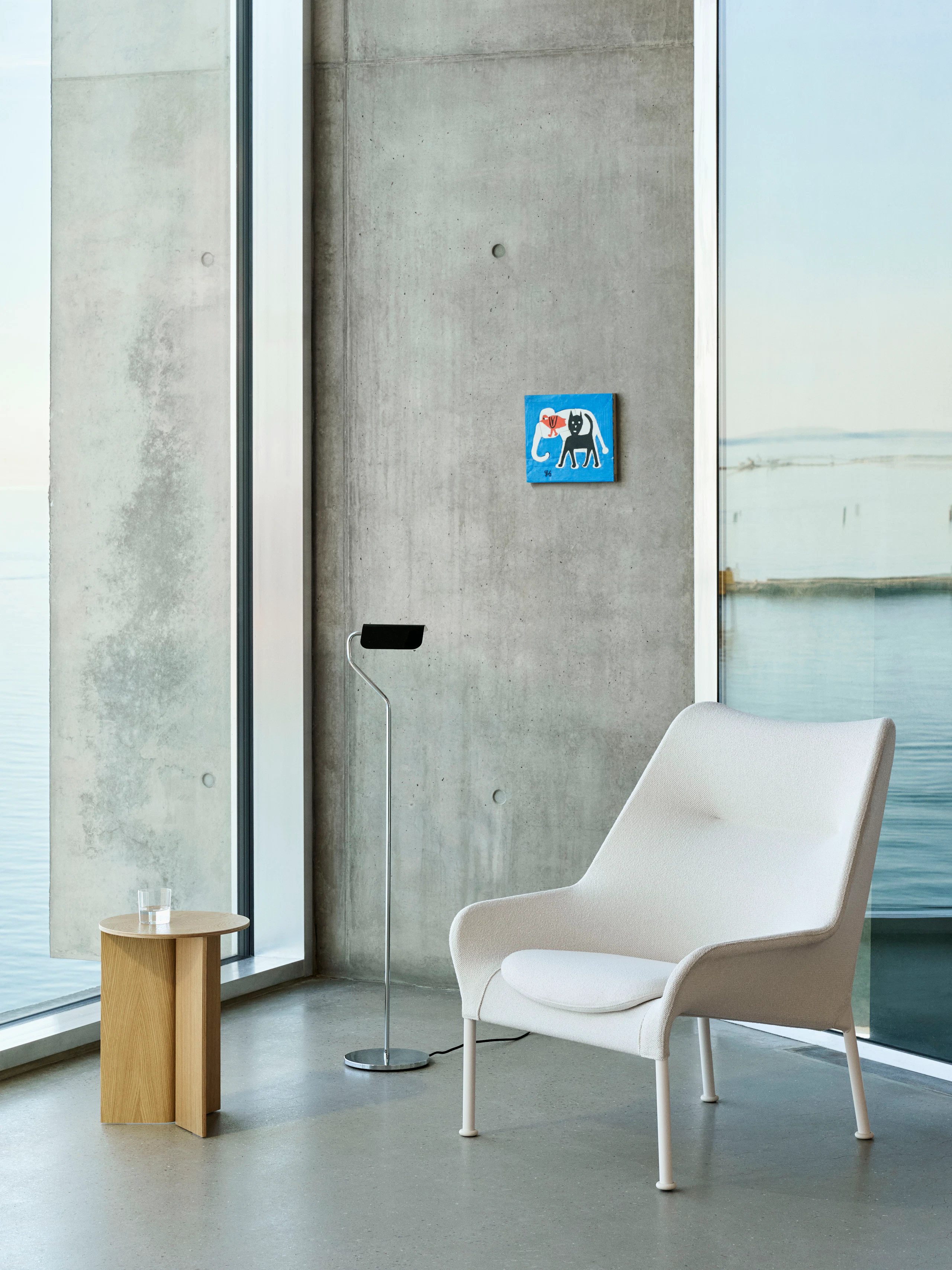 O2 Lounge Chair and Wood Slit Table staged in a concrete and glass lobby with artwork on the wall.