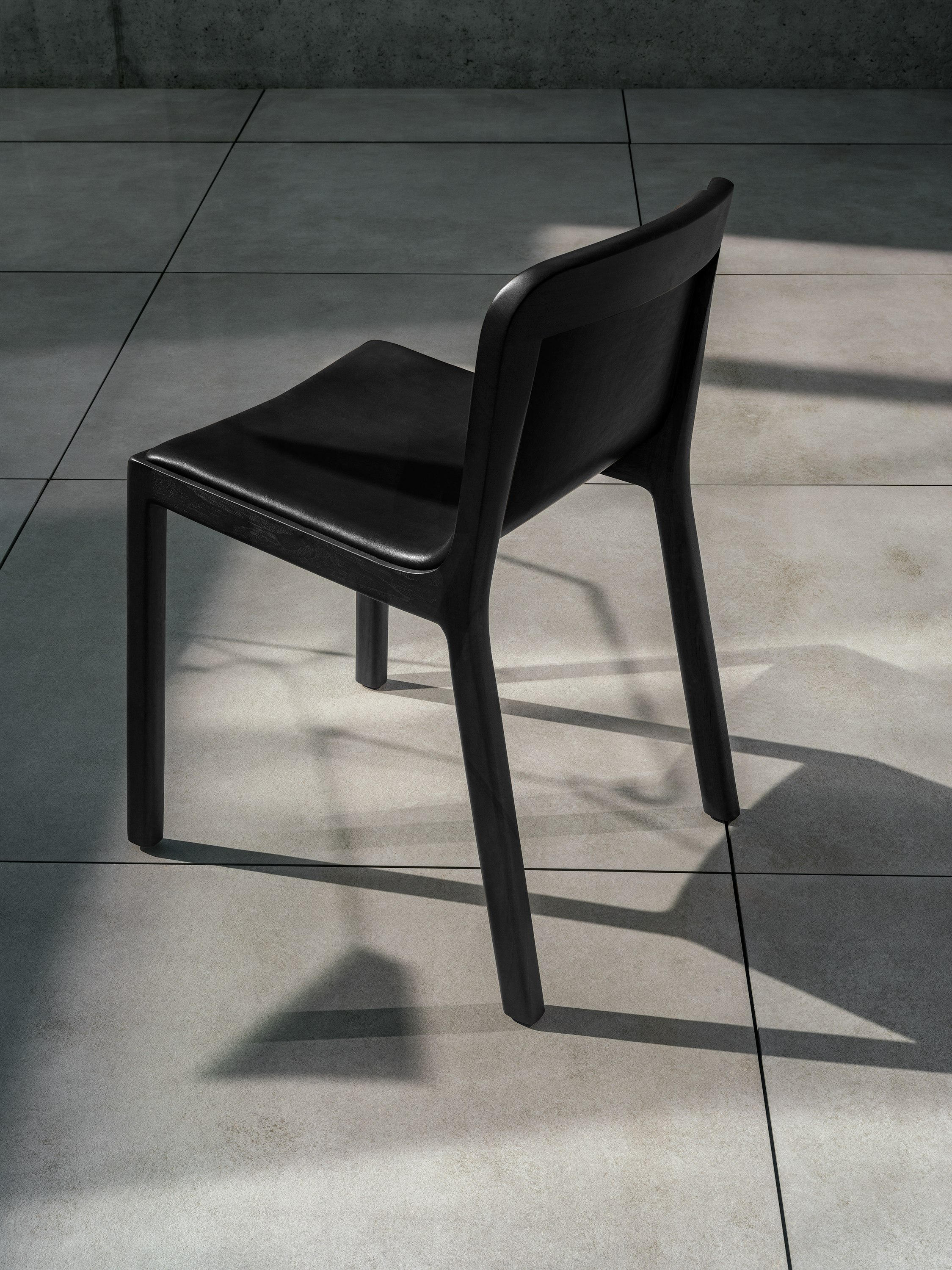 Lijn Side Chair in Ebonized Oak fully upholstered with black leather, viewed from behind at an angle on concrete.
