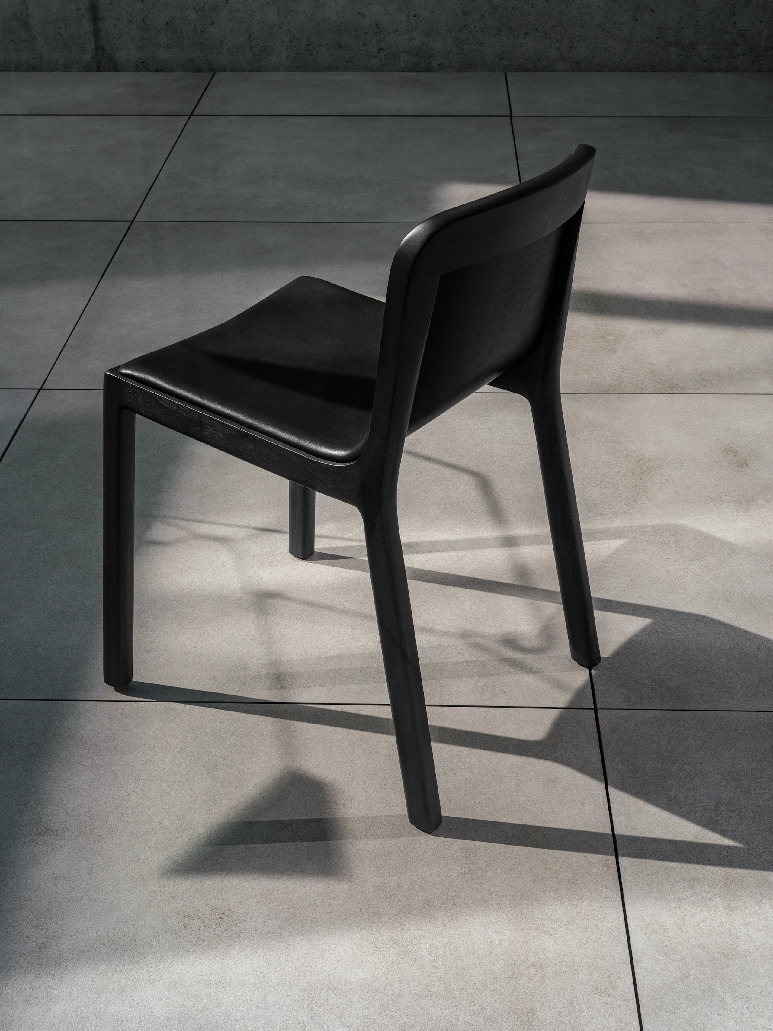 Lijn Side Chair in Ebonized Oak fully upholstered with black leather, viewed from behind at an angle on concrete.