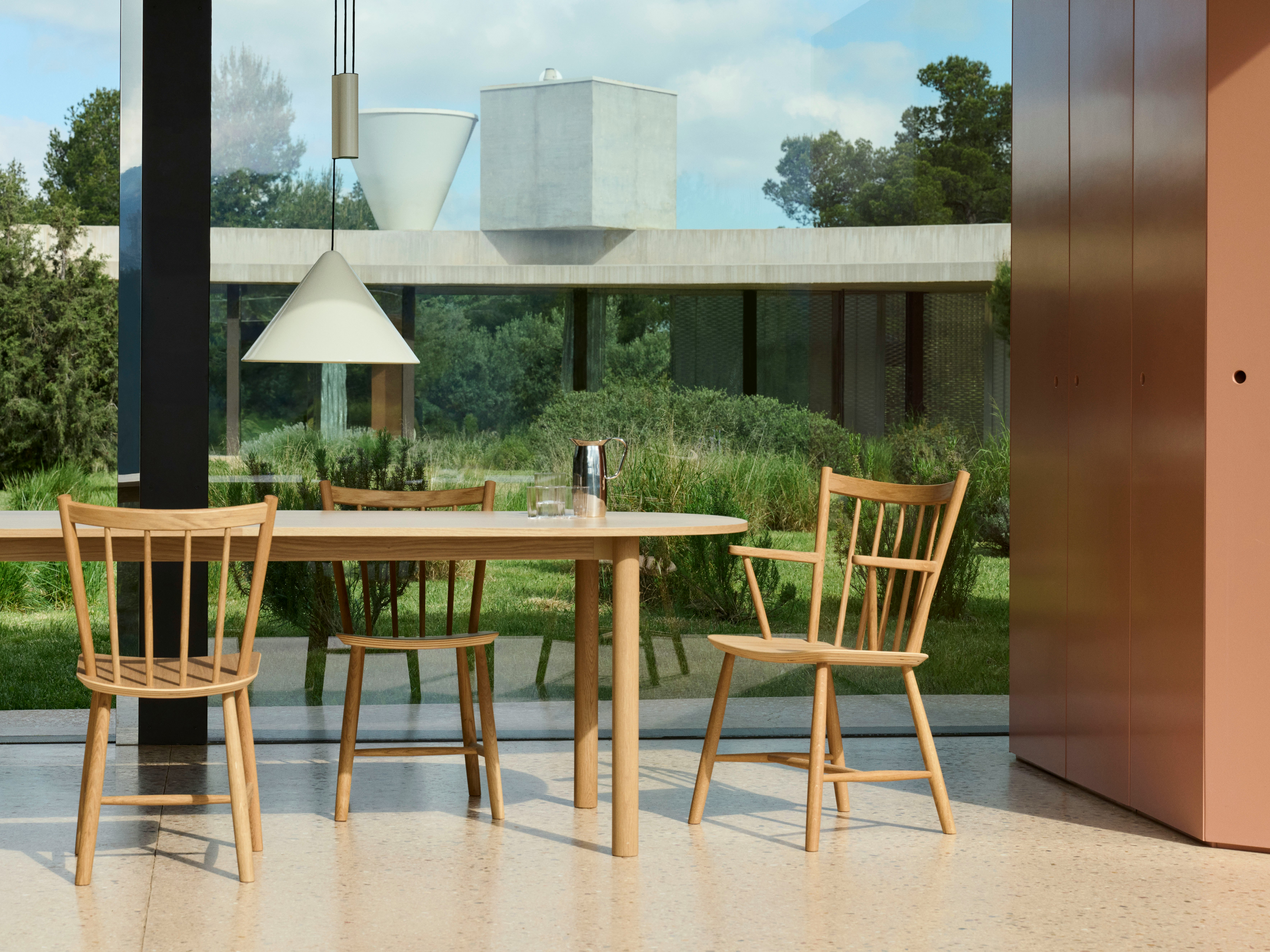Annex Table oblong with wood legs and natural oak top staged outdoors near glass walls.