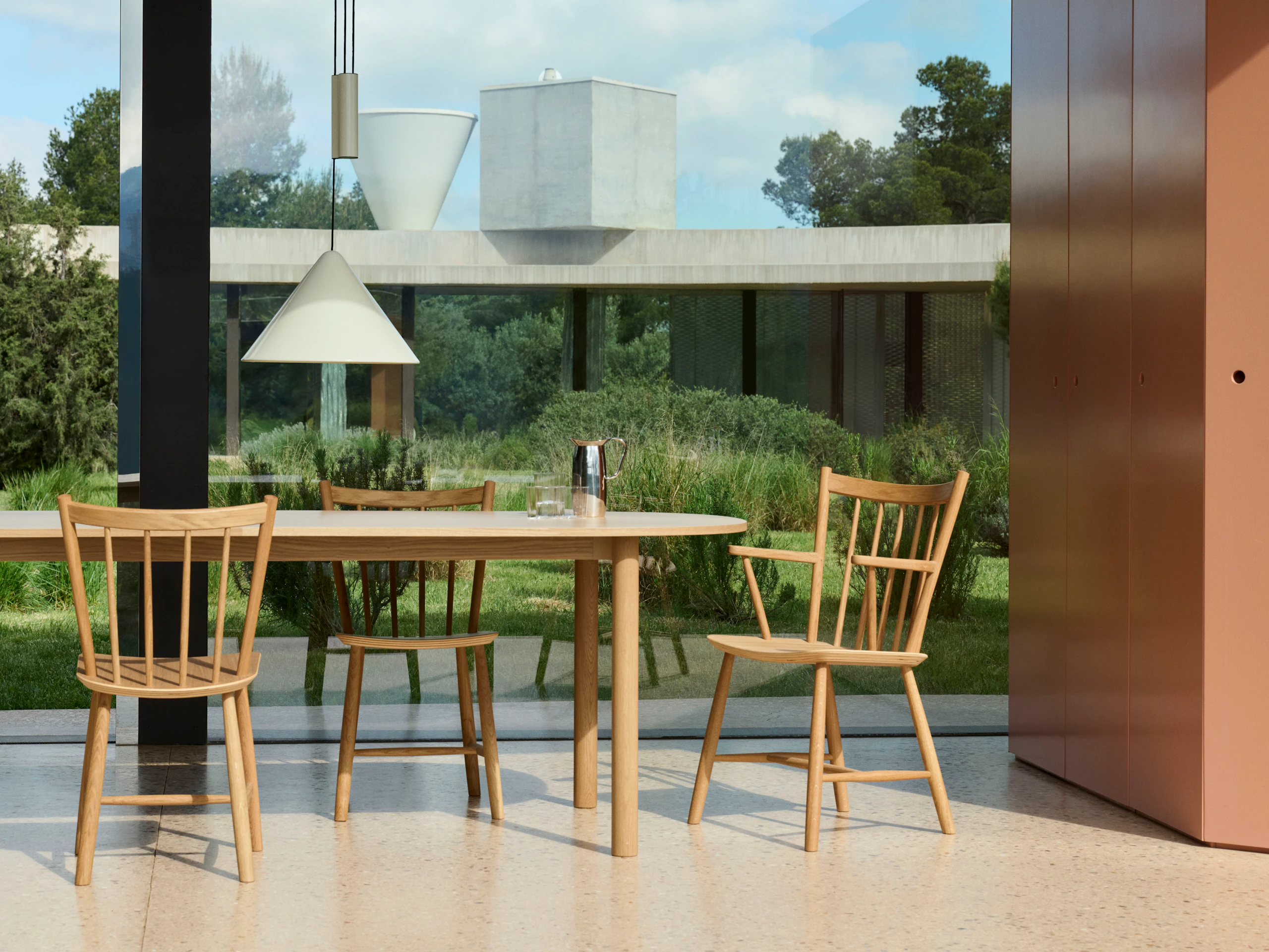 Annex Table oblong with wood legs and natural oak top staged outdoors near glass walls.