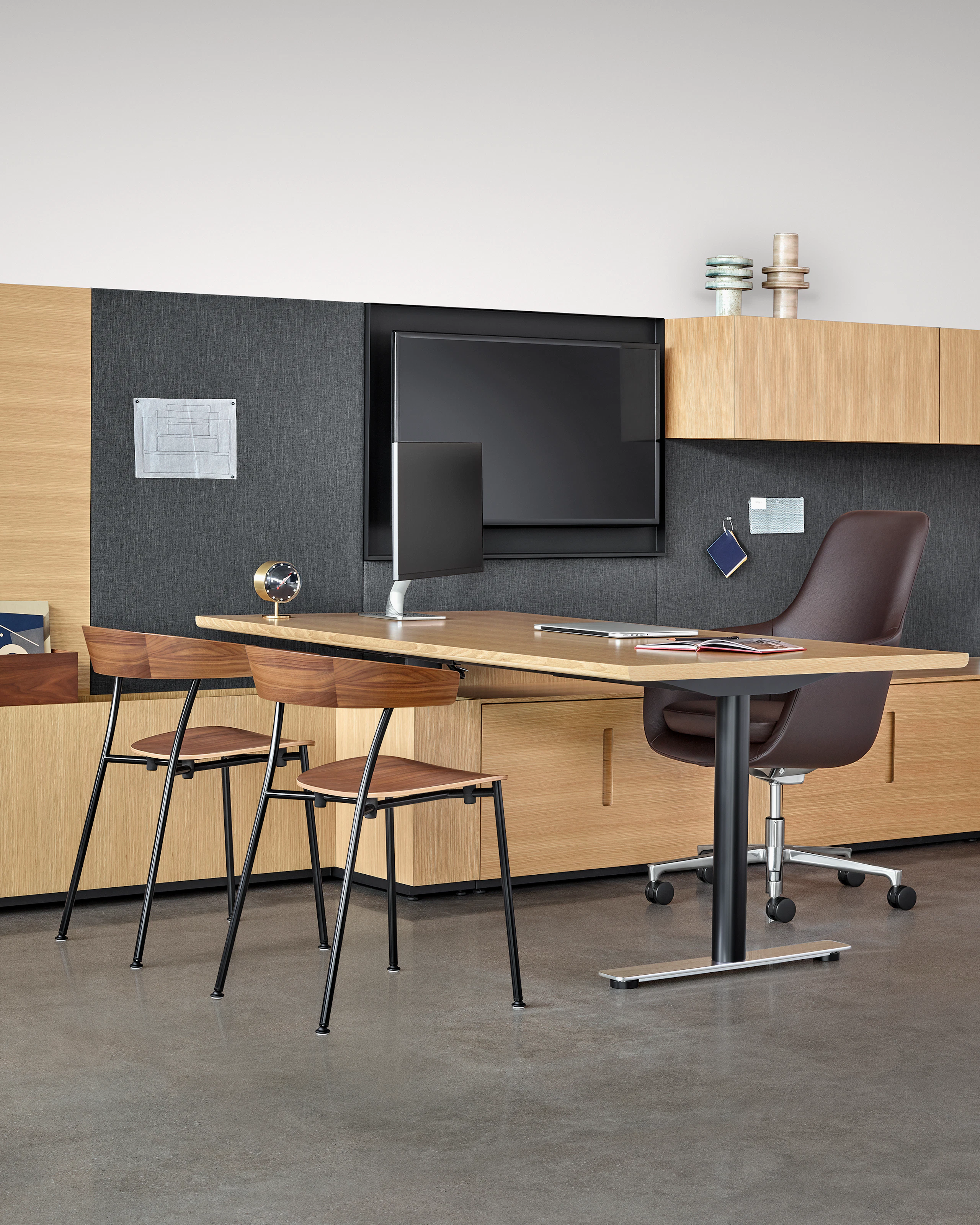 Two Leeway side chairs face a black leather Saiba office chair with a rectangular desk between. Select to go to the All Seating landing page.