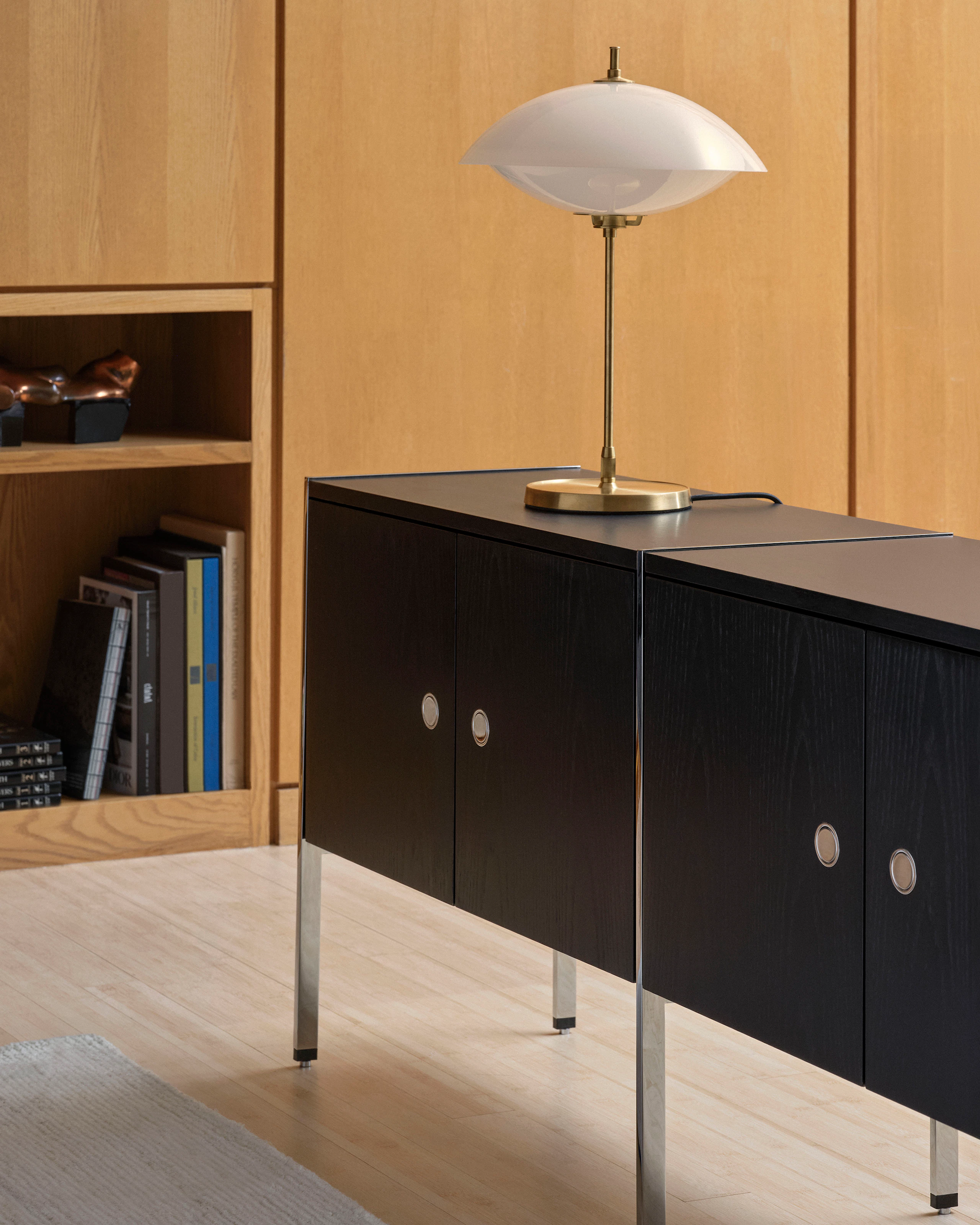 H Frame Credenza in Ebonized Ash with chrome frame styled with a lamp, viewed at an angle in a library setting.