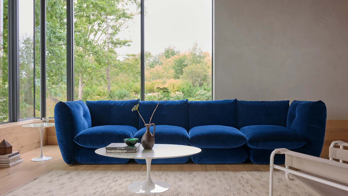 Blue modular sofa in a bright living room with large windows and round white coffee table