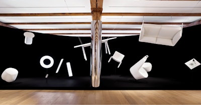 A variety of white furniture suspended from the ceiling in front of a large black sheet at the NaughtOne showroom at MillerKnoll Design Days