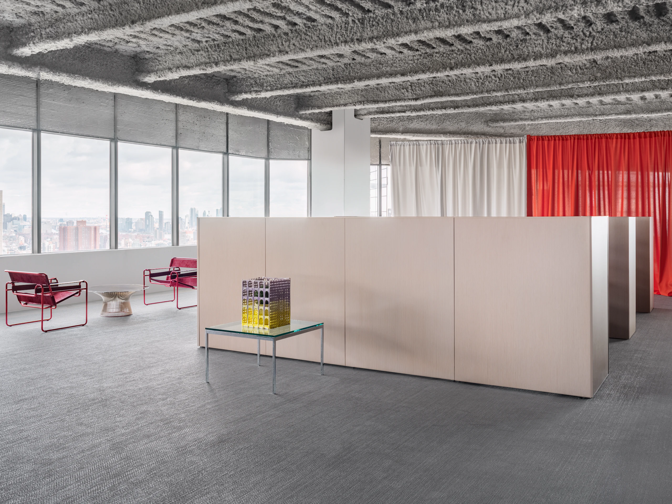 The panel system of a group of workstations are visible in an open office space along with a few end tables and lounge chairs.