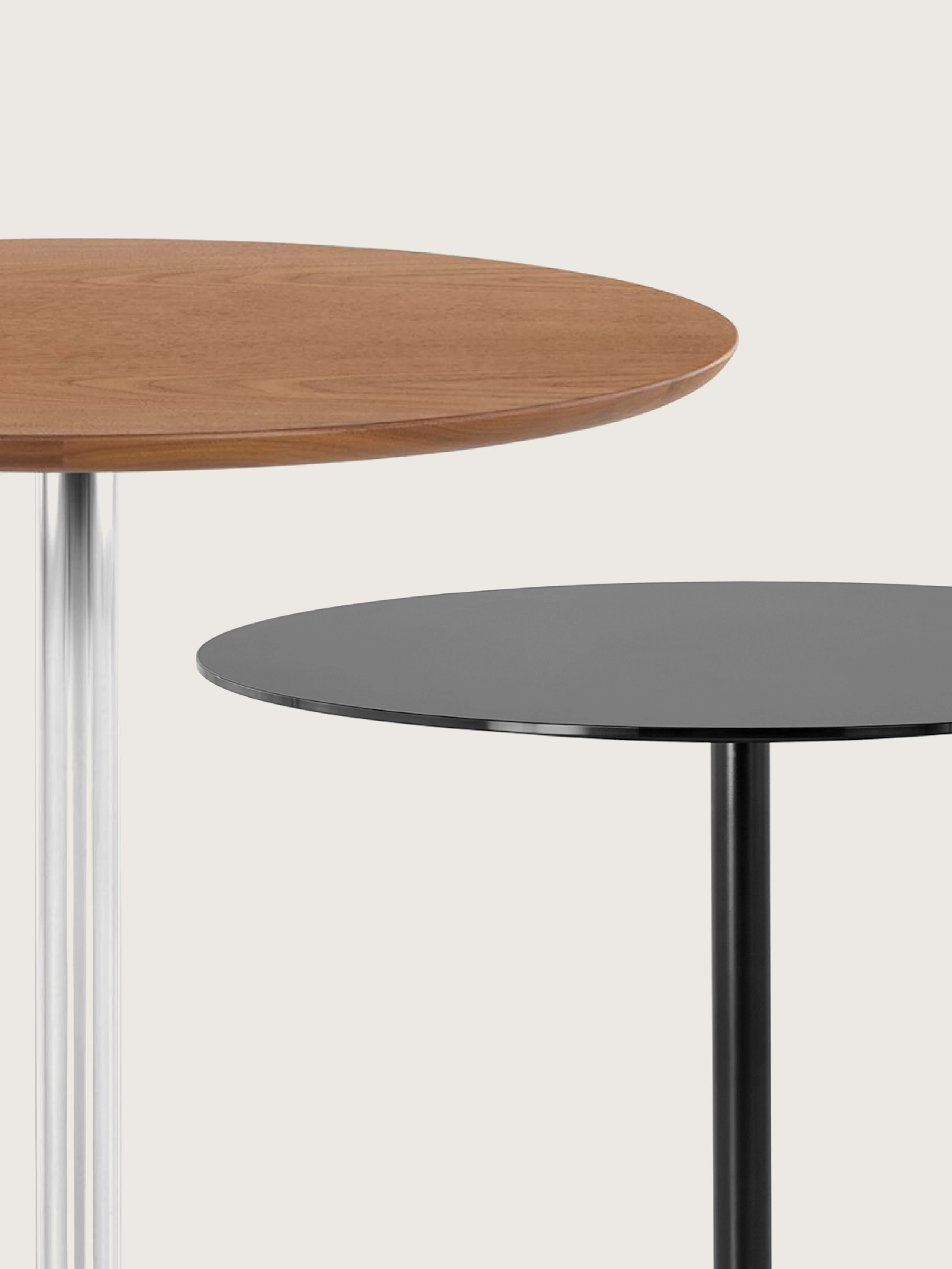 Close-up of two Saiba Tables staggered, one with a Walnut tabletop and a chrome base, one in all black, with only partial tabletops and columns visible, on a white sweep.