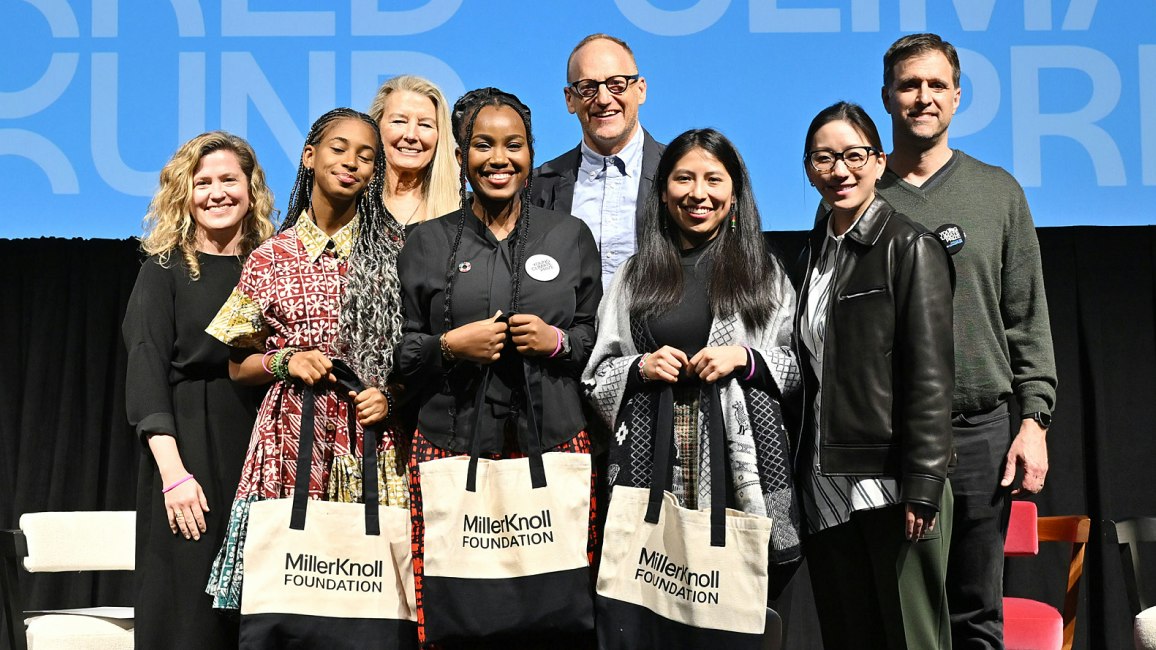 A group of people stand on a stage. Three young women hold black and white MillerKnoll Foundation tote bags.
