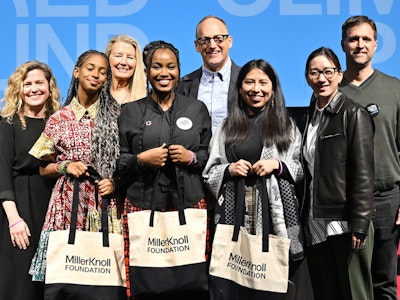A group of people stand on a stage. Three young women hold black and white MillerKnoll Foundation tote bags.