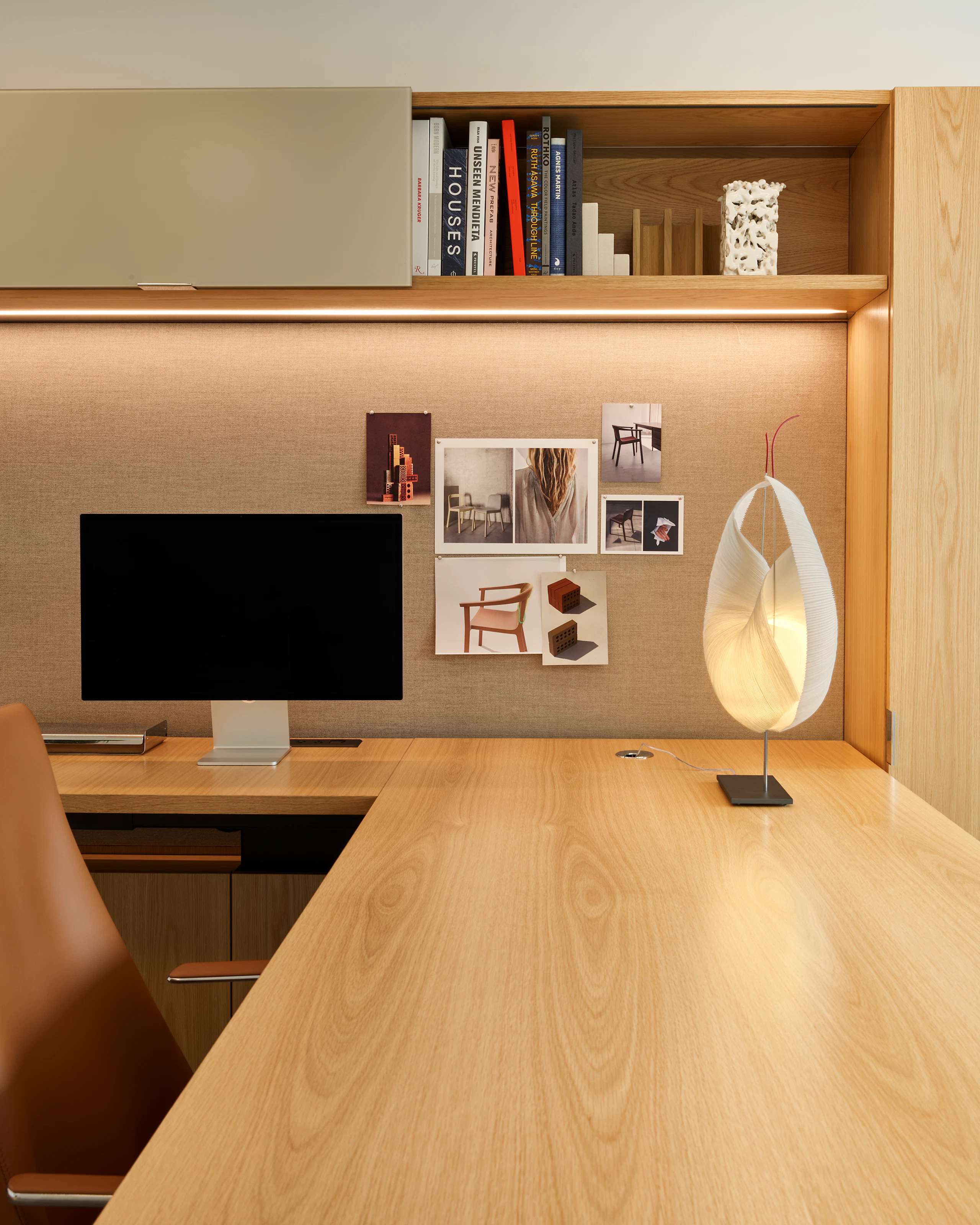 Geiger One Casegoods in Natural Flat Cut Oak with a Geiger Taper Chair by Mark Goetz viewed from the side with office accessories including a table lamp and books in overhead storage, in a private office in the Geiger Chicago Showroom.