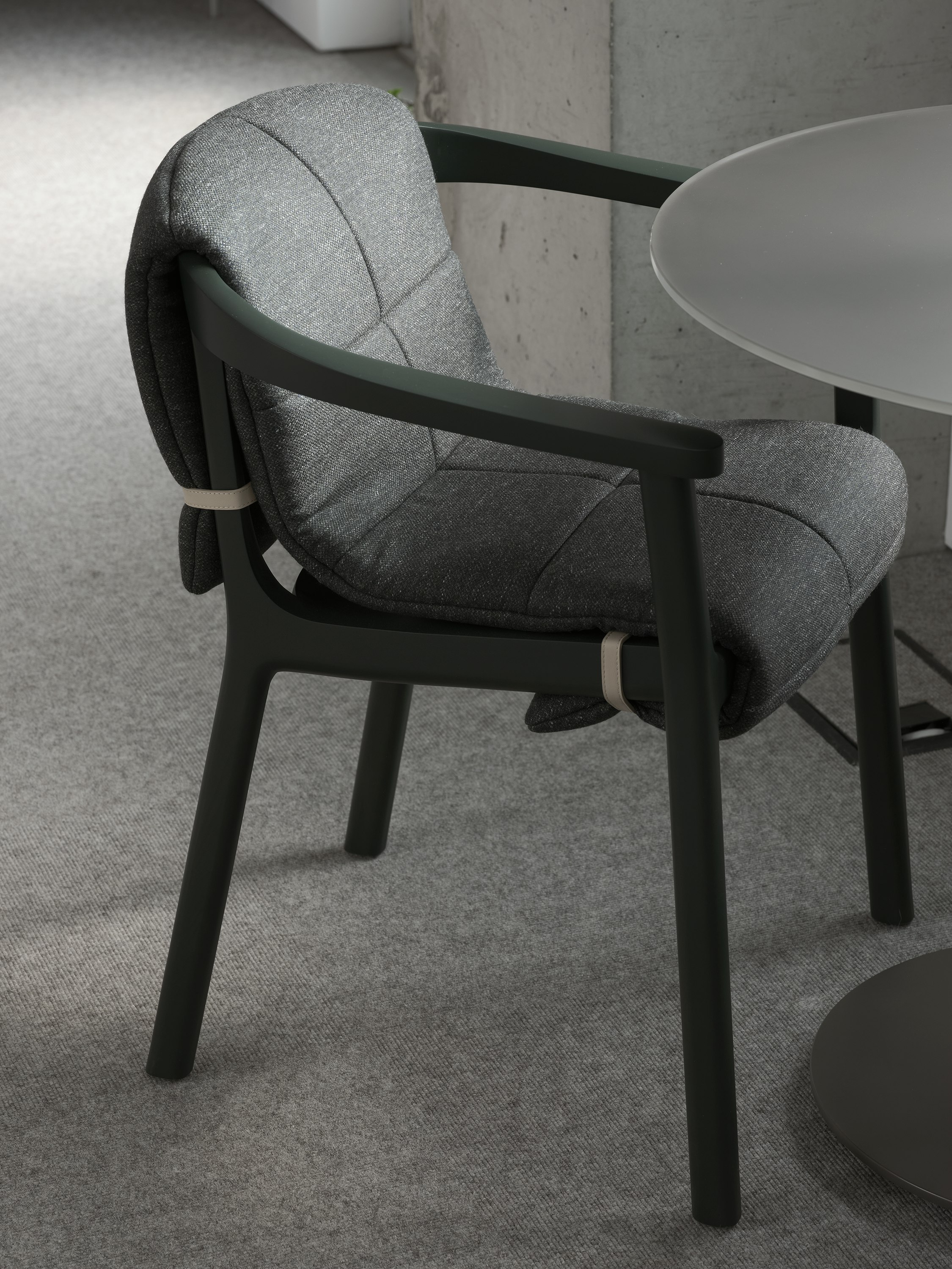 Lijn Armchair in Ivy with a quilted wrap in Bellano Black Green viewed at an angle next to a cafe table in a showroom setting.