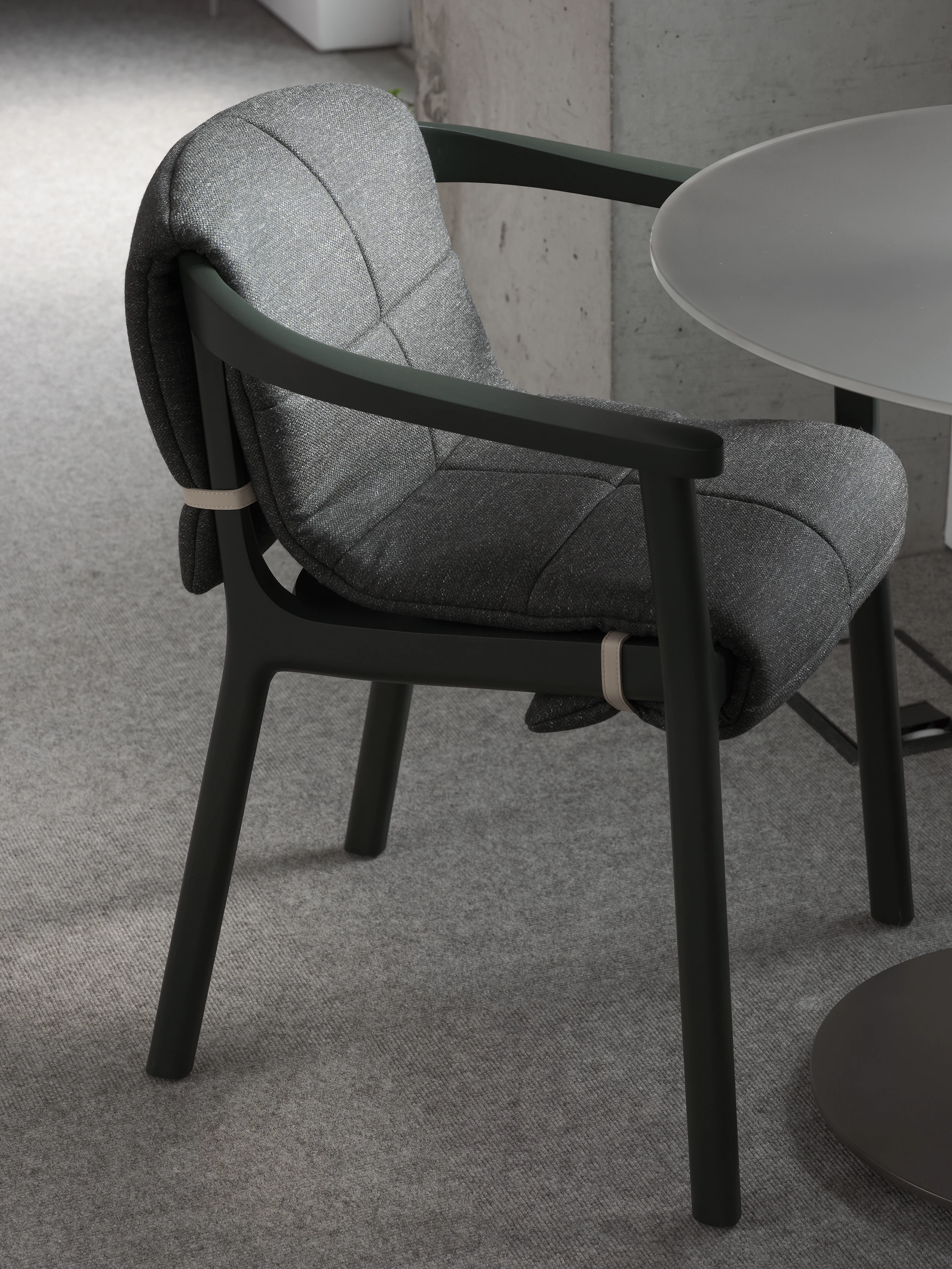 Lijn Armchair in Ivy with a quilted wrap in Bellano Black Green viewed at an angle next to a cafe table in a showroom setting.