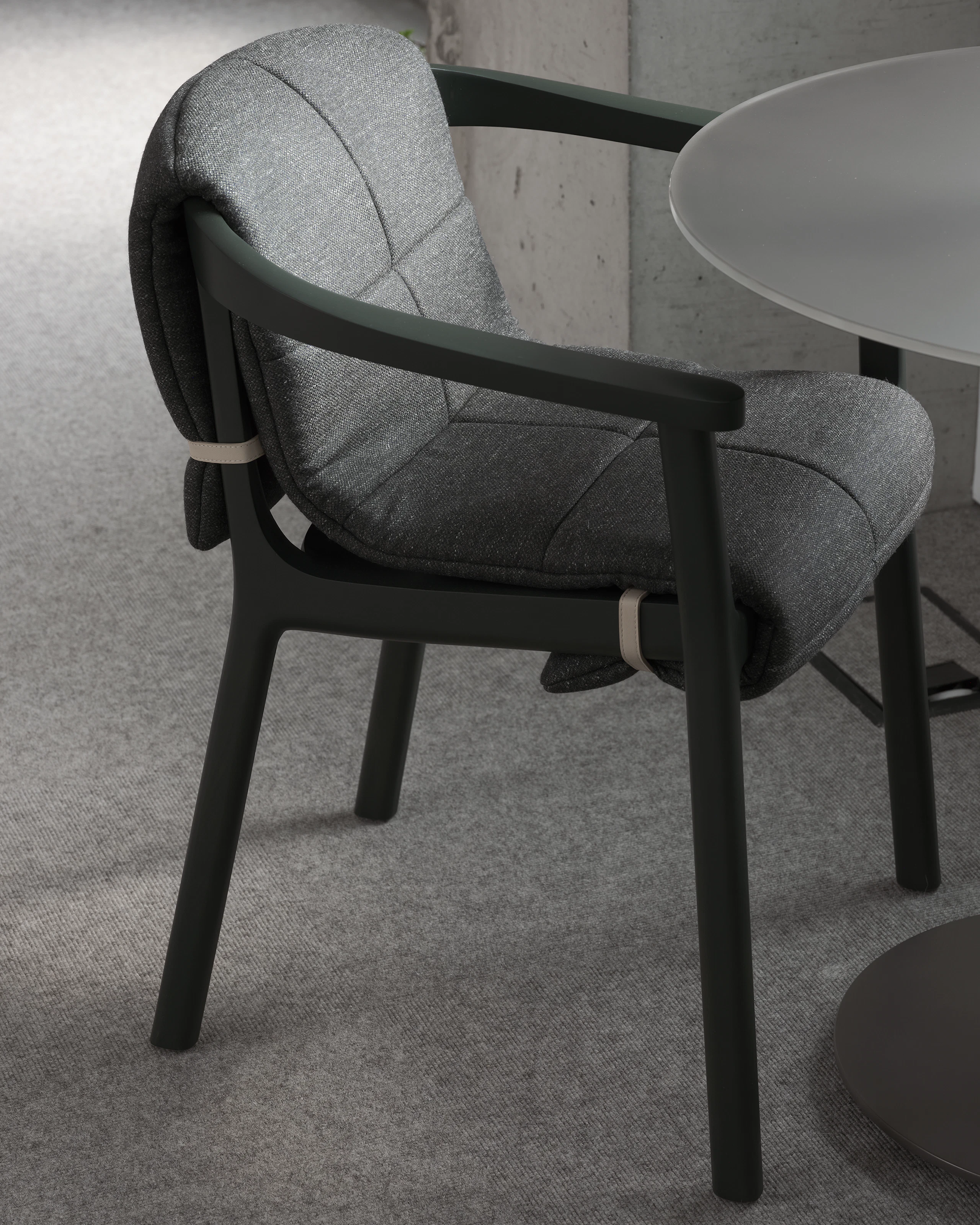 Lijn Armchair in Ivy with a quilted wrap in Bellano Black Green viewed at an angle next to a cafe table in a showroom setting.