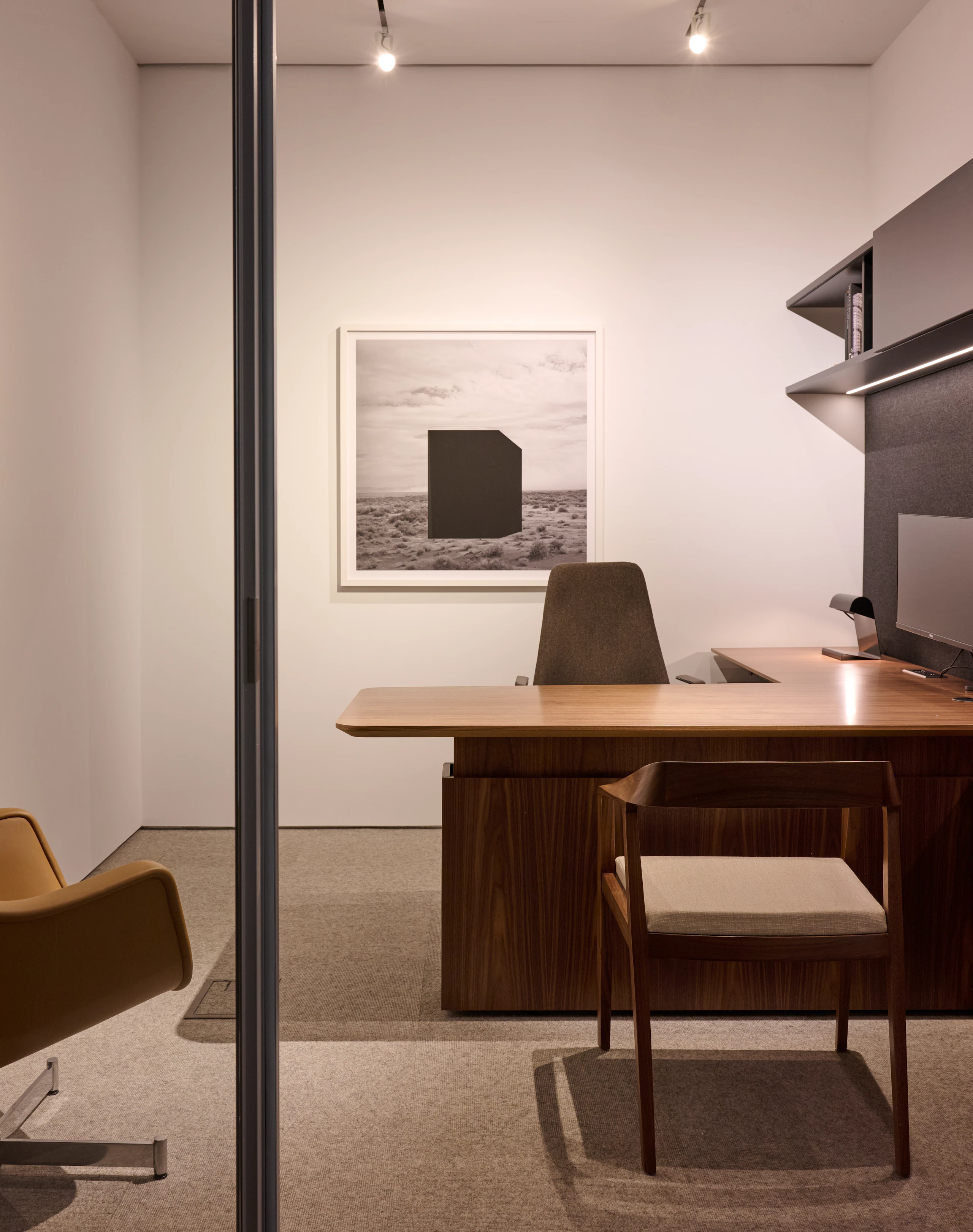 Geiger One Private Office in Natural Flat Cut Walnut with a height adjustable L-shaped work surface, a Full Twist Chair and Bumper Lounge Chair for guests, and a Taper Chair, viewed from the front.