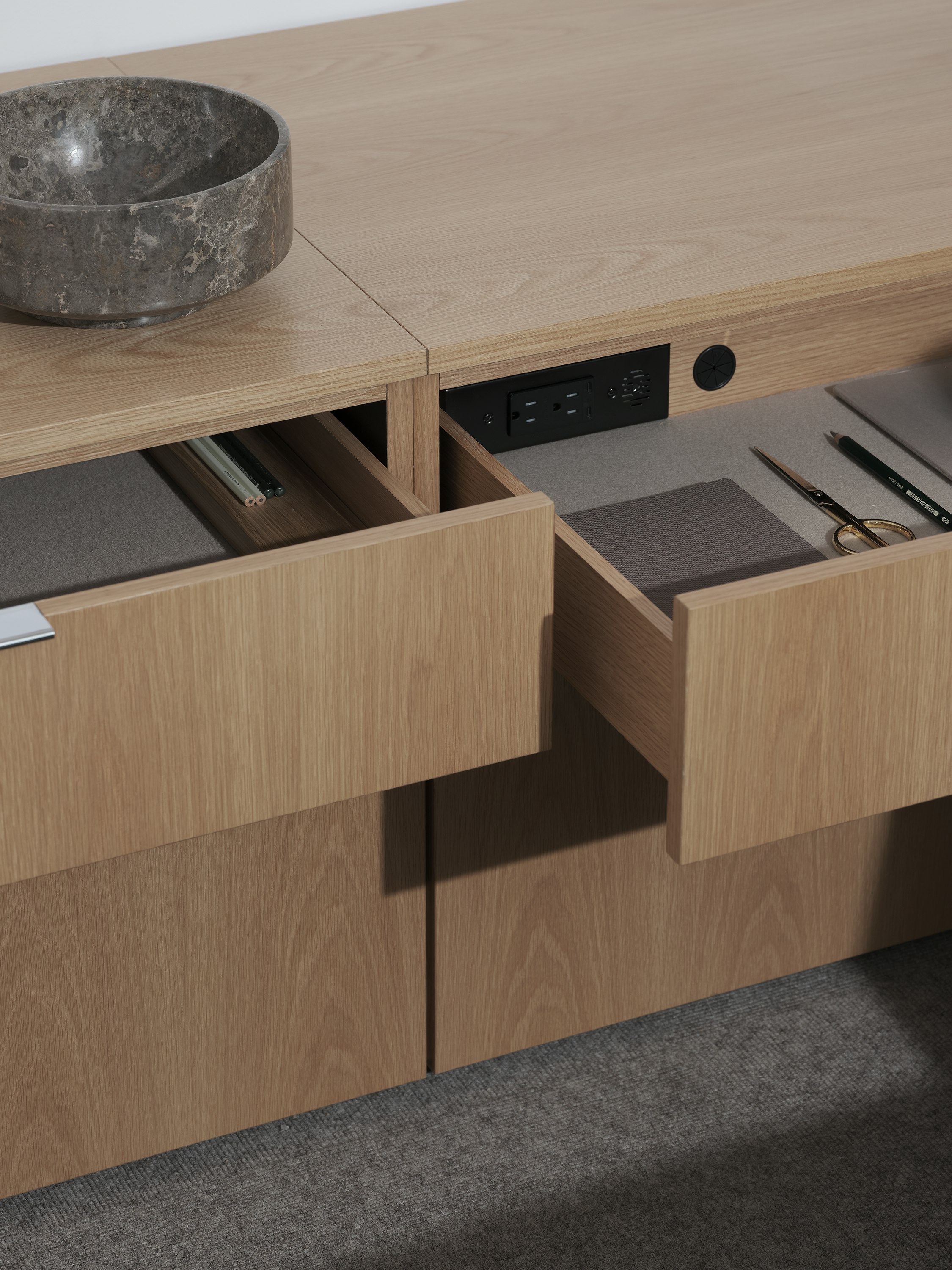 Detail view of two open felt-lined Geiger One Private Office storage drawers in Natural Flat Cut Oak, one with in-drawer power access, viewed at an angle.