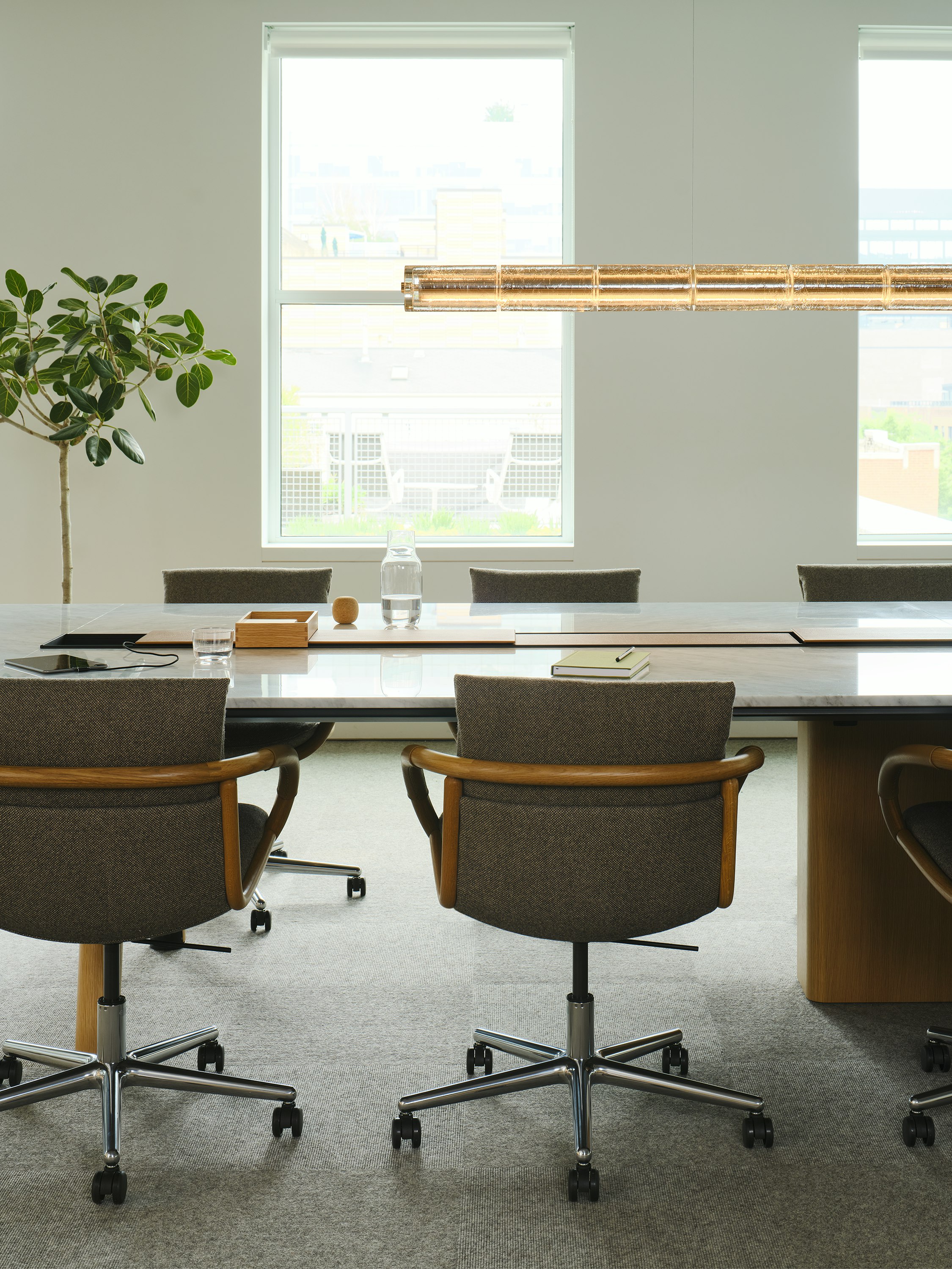 Close up view of the Ascent Conference Table in White Carrara Marble and Natural Rift Cut Oak with Full Loop Chairs in Oak with grey upholsery, both designed by EOOS, in a conference room setting.