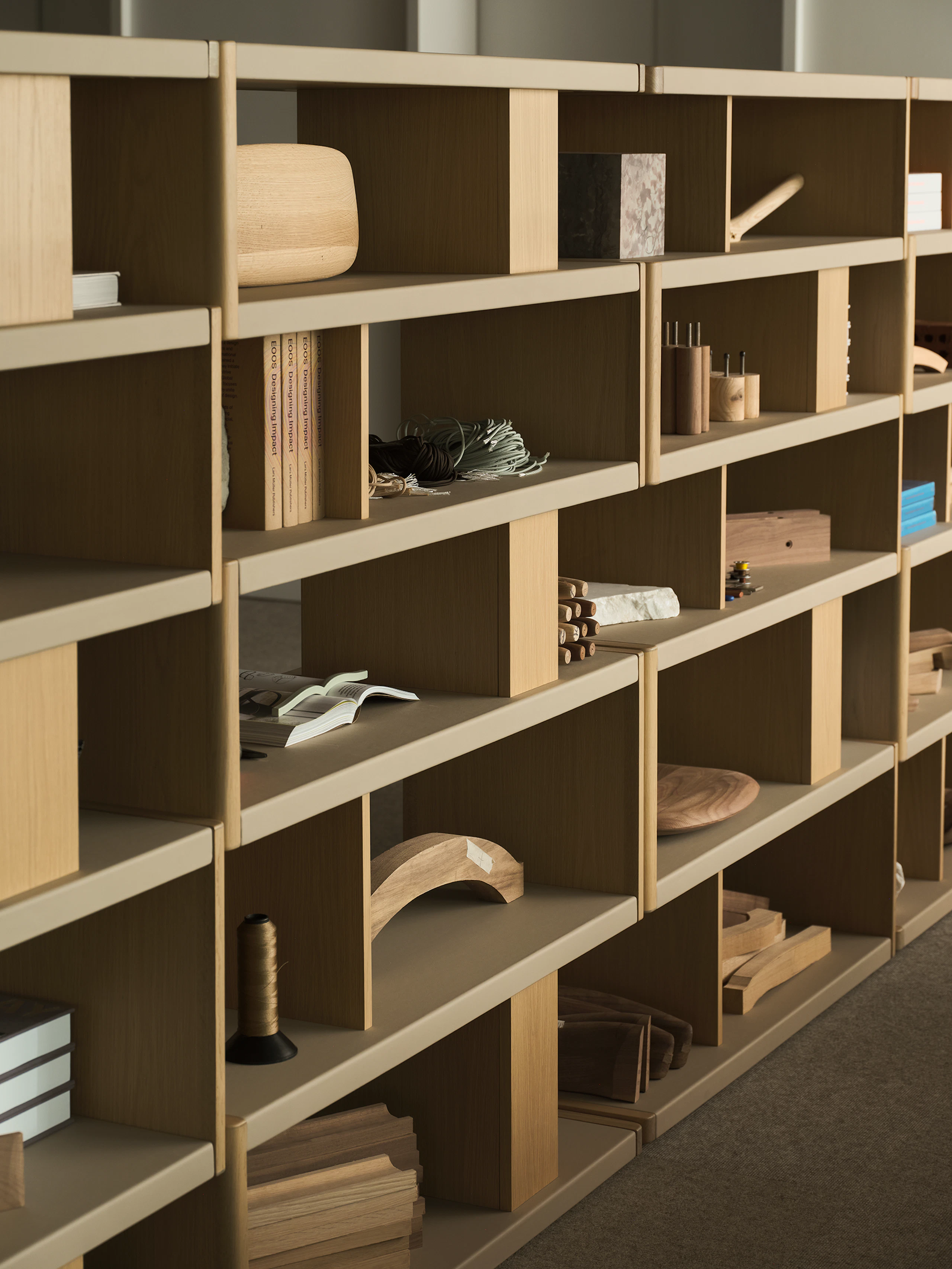 Various New Canaan Tall Bookshelves in Light Oak wrapped with Bristol Leather in Champagne arranged side by side and styled with various objects, viewed at an angle.