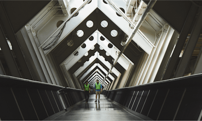 Two people in high-visibility vests walking down a long pathway at a Herman Miller manufacturing facility in Michigan.