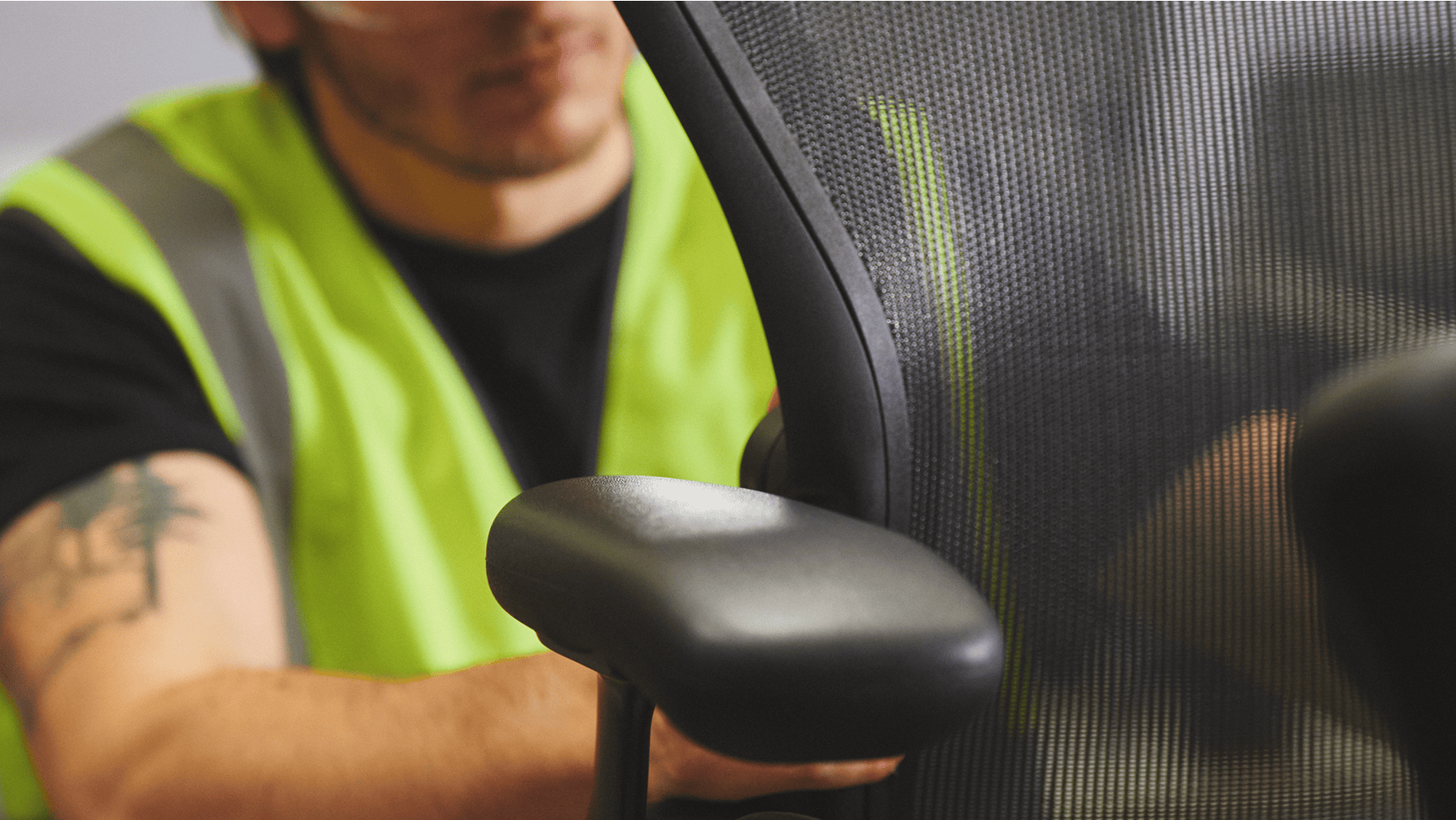 A man in a high-visibility work vest assembling a black Aeron Chair by Herman Miller.