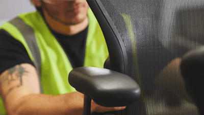 A man in a high-visibility work vest assembling a black Aeron Chair by Herman Miller.