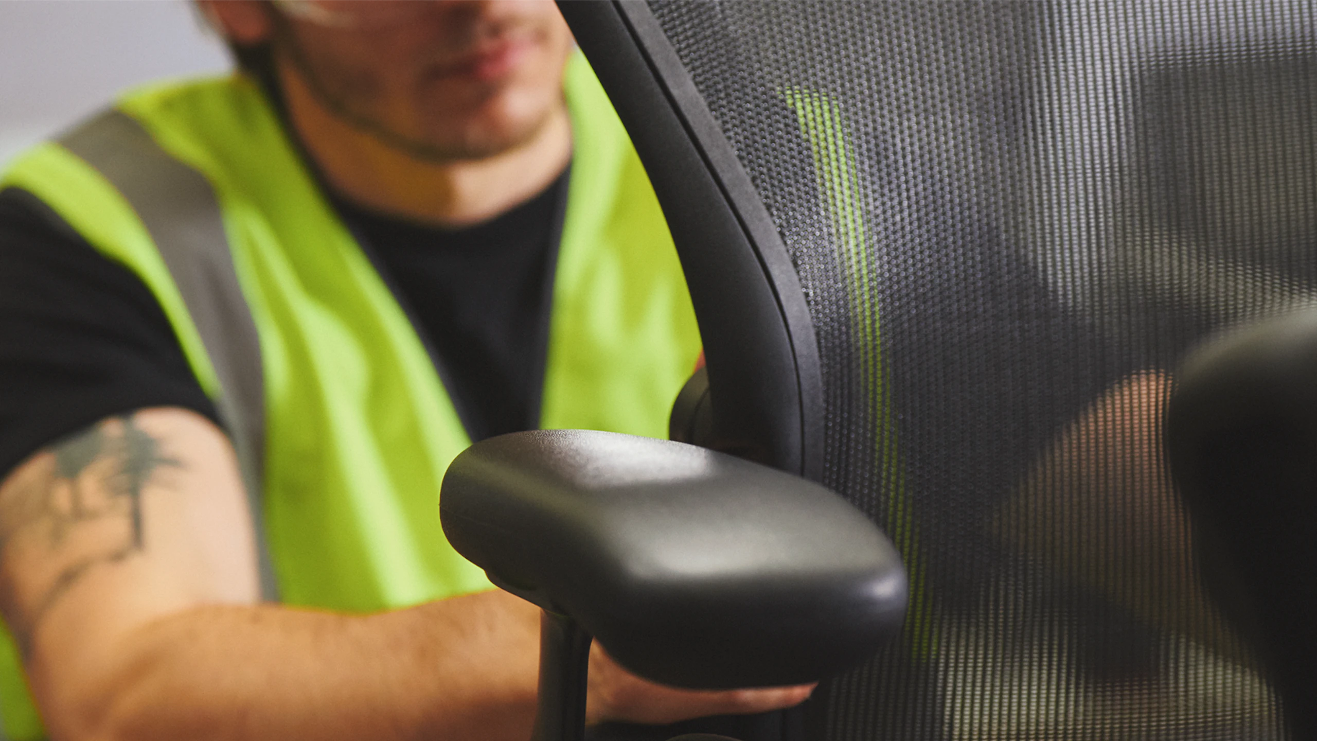 A man in a high-visibility work vest assembling a black Aeron Chair by Herman Miller.