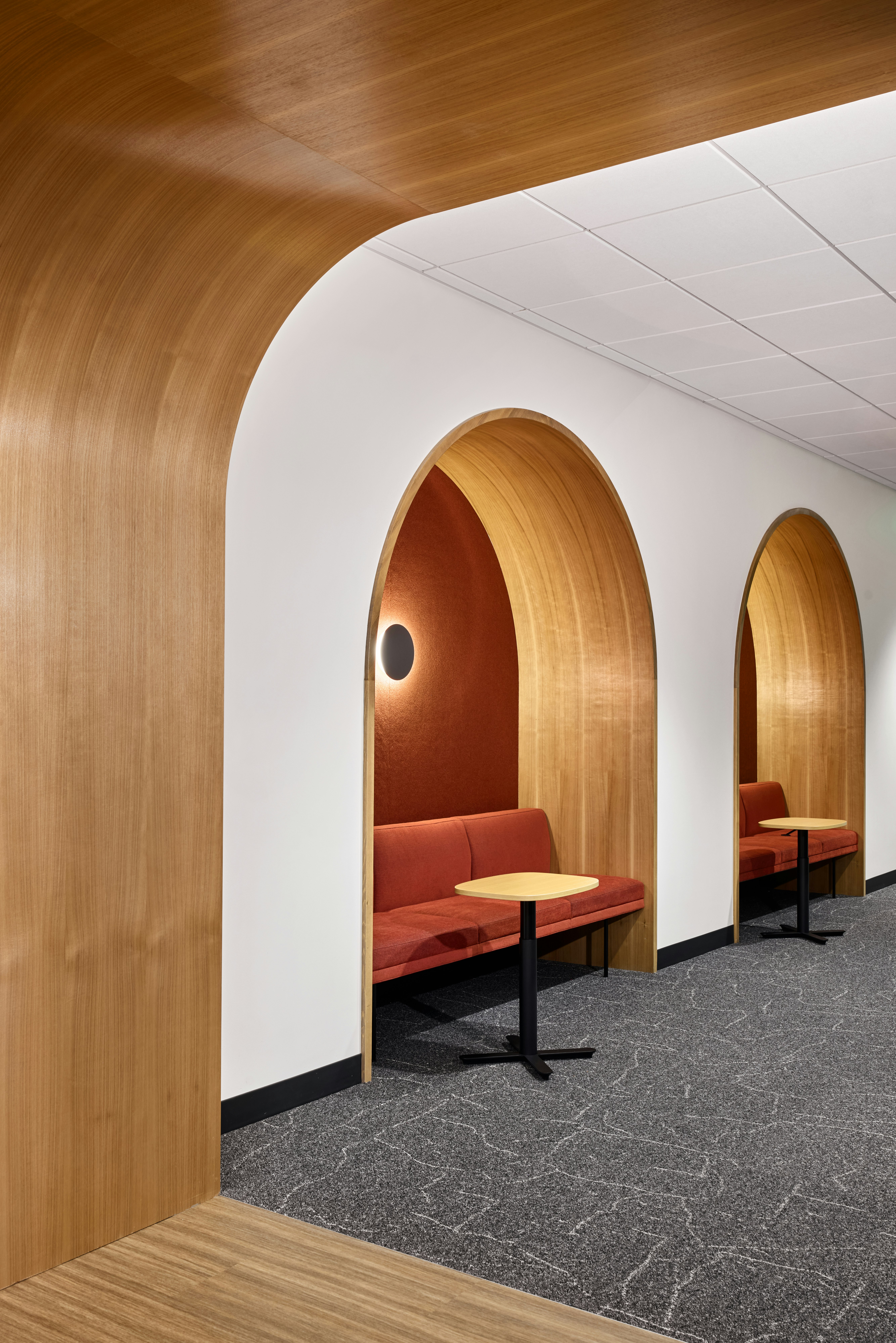  Wood-accented corridor with arched upholstered alcoves, integrated lounge seating, and Herman Miller Passport Tables.