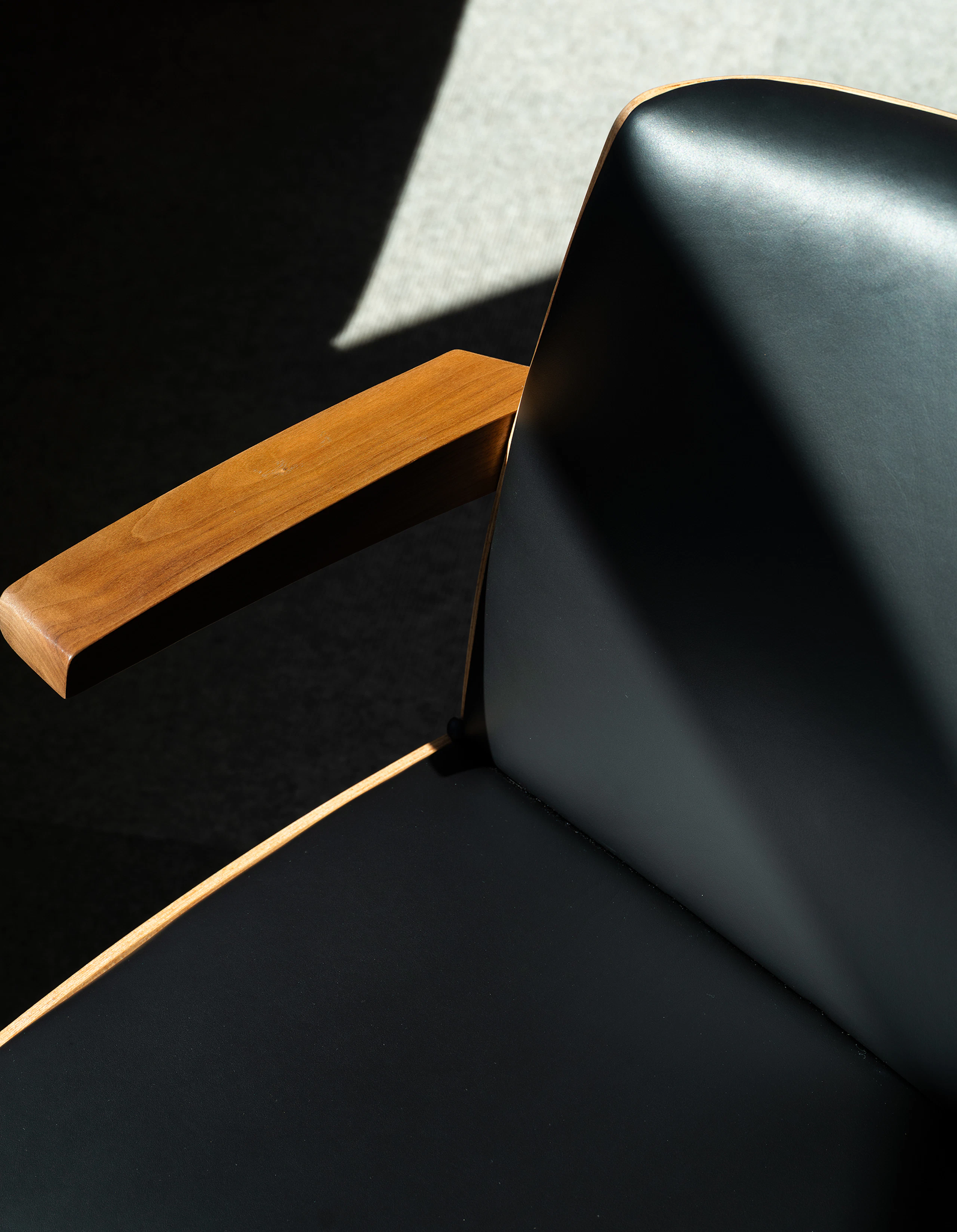 Detail view of a low back Clamshell Conference Chair in Walnut upholstered with black leather, viewed from above.