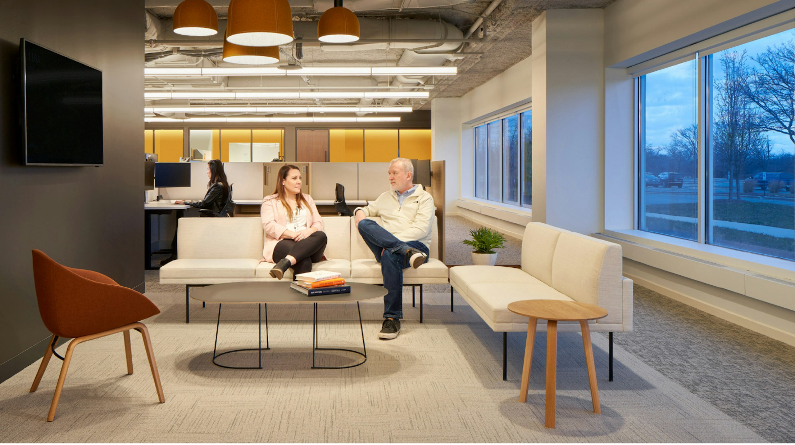 Two people having a conversation while sitting on a white, three-seat sofa in communal seating area in an industrial organization's office