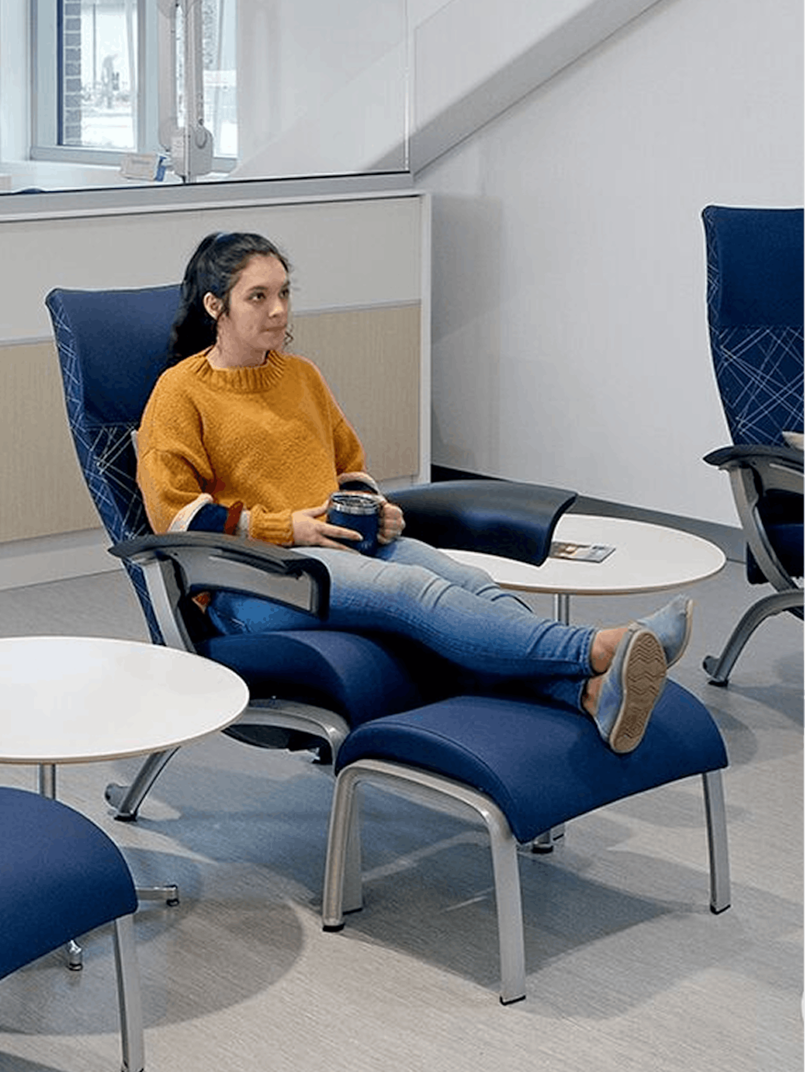 A person in a yellow sweater sitting in a blue Nemschoff Nala Patient Chair in a waiting area at BAMF Health in Michigan